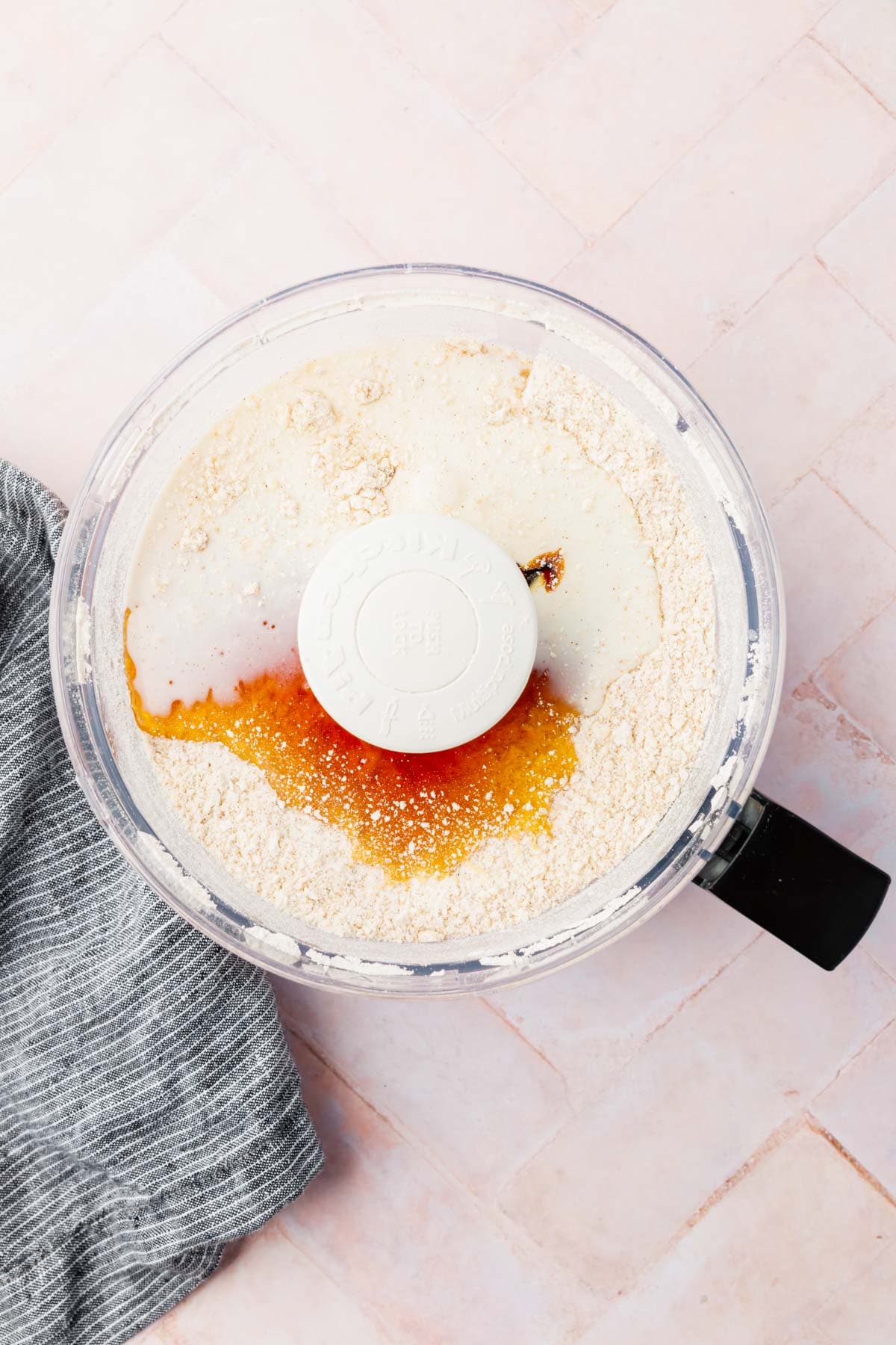 A food processor with gluten-free flour, honey, milk and vanilla extract in it. 