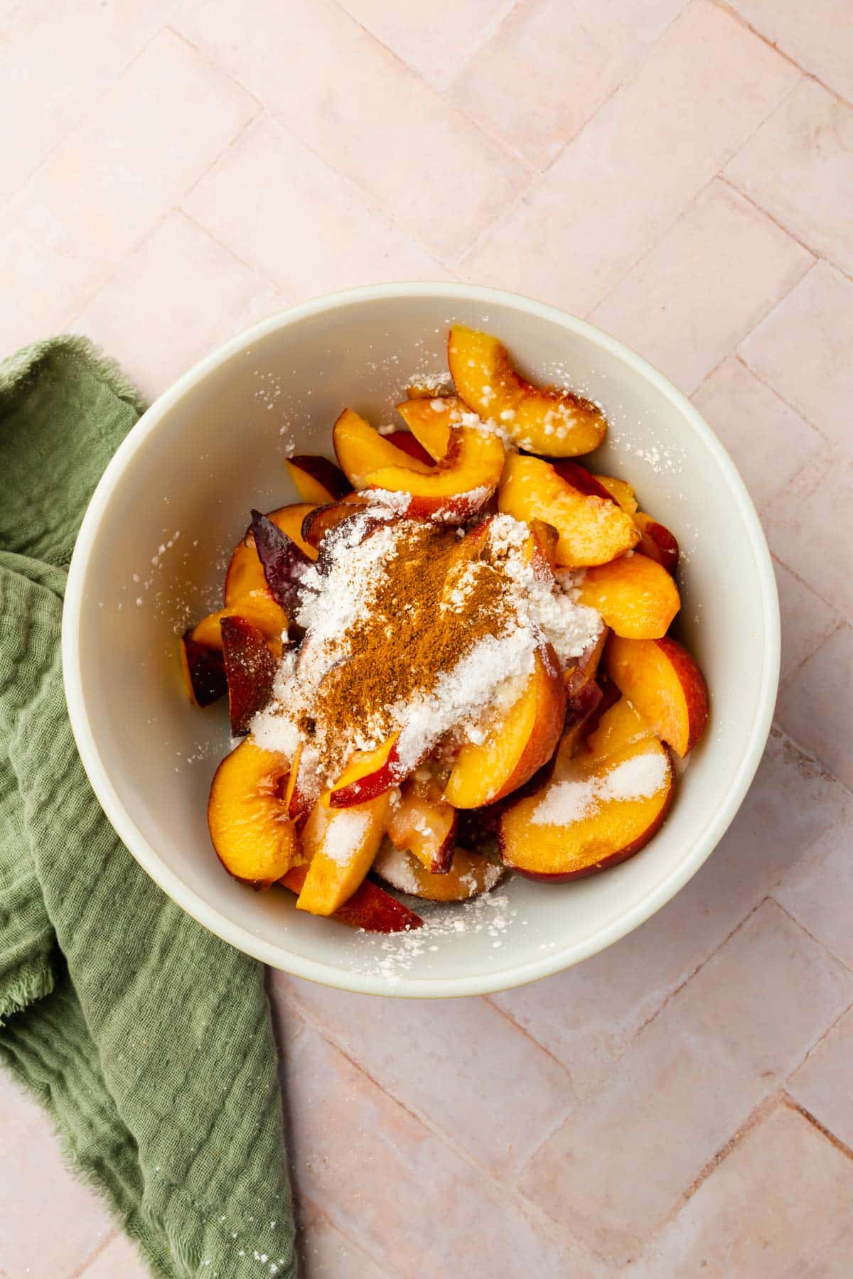 A bowl of sliced peaches, cornstarch, cinnamon, lemon juice, nutmeg, and granulated sugar ready to be mixed together.