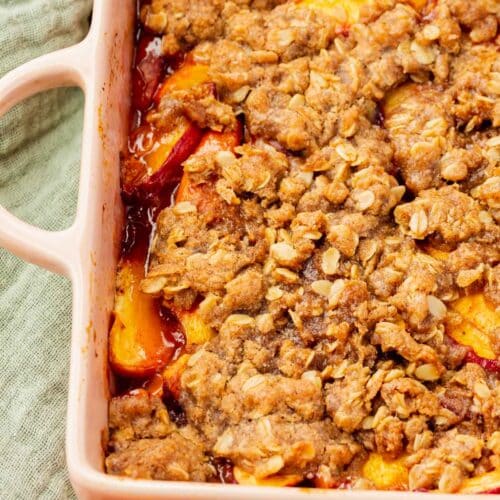 A close up of gluten-free vegan peach crisp in a square pink baking dish.