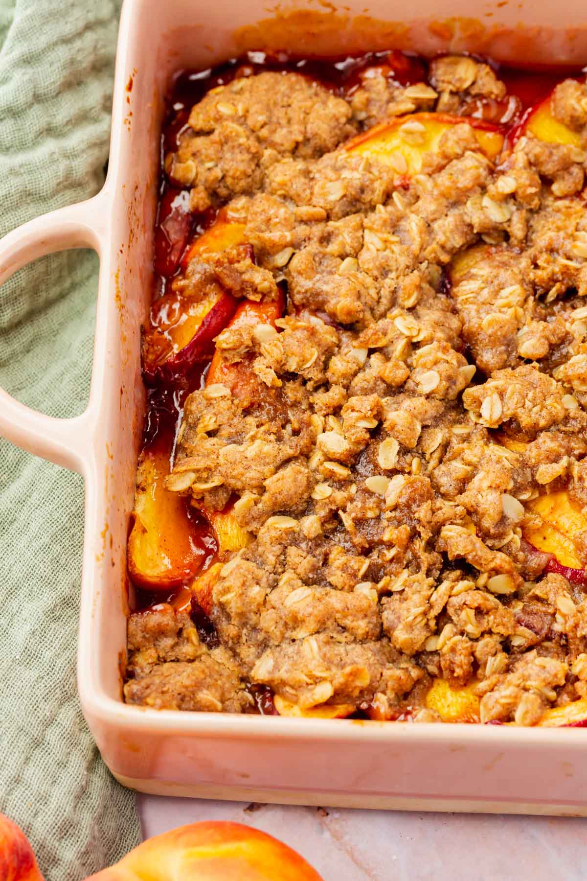 A close up of gluten-free vegan peach crisp in a square pink baking dish.