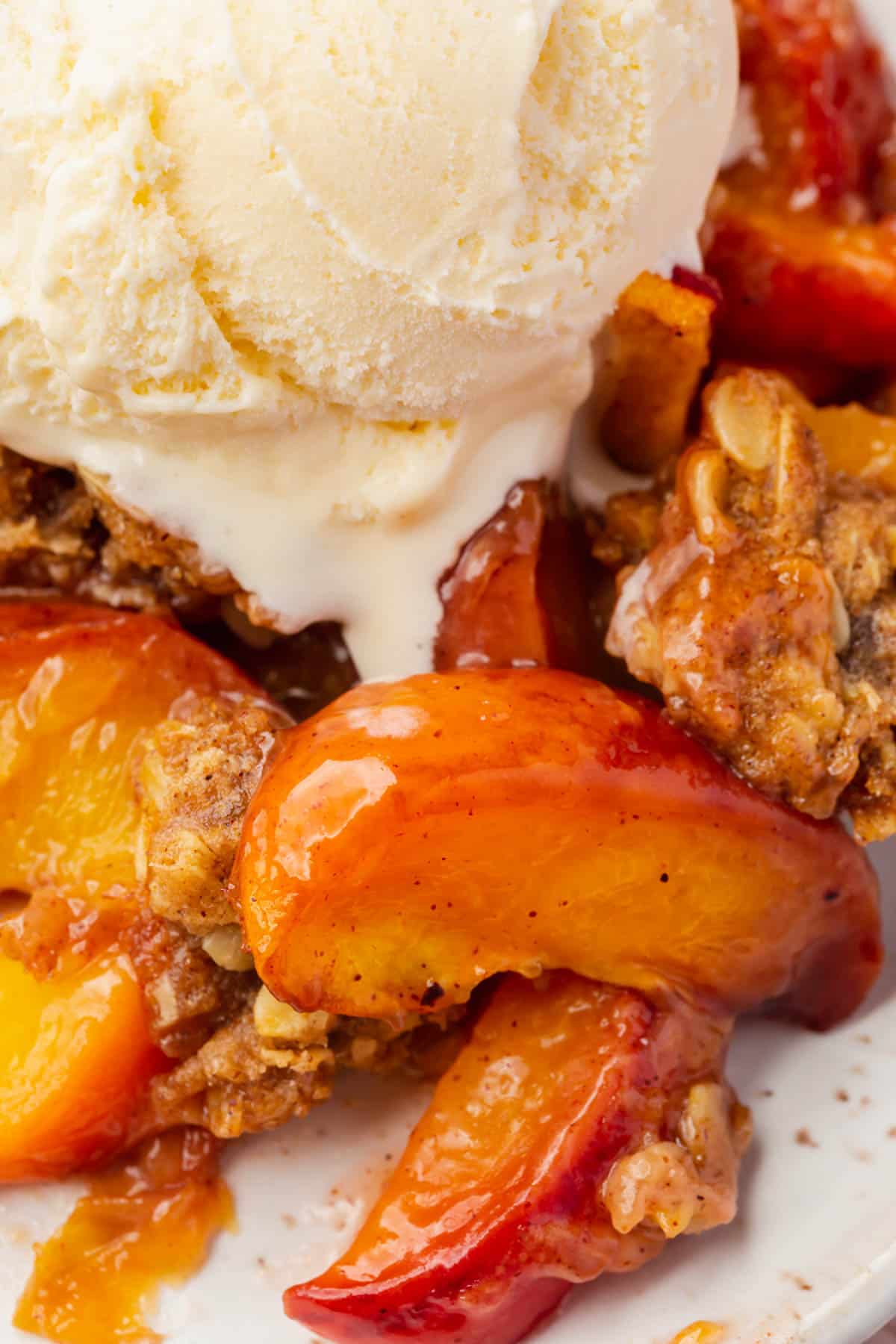 A close up of gluten-free peach crisp with a scoop of vanilla ice cream on top.