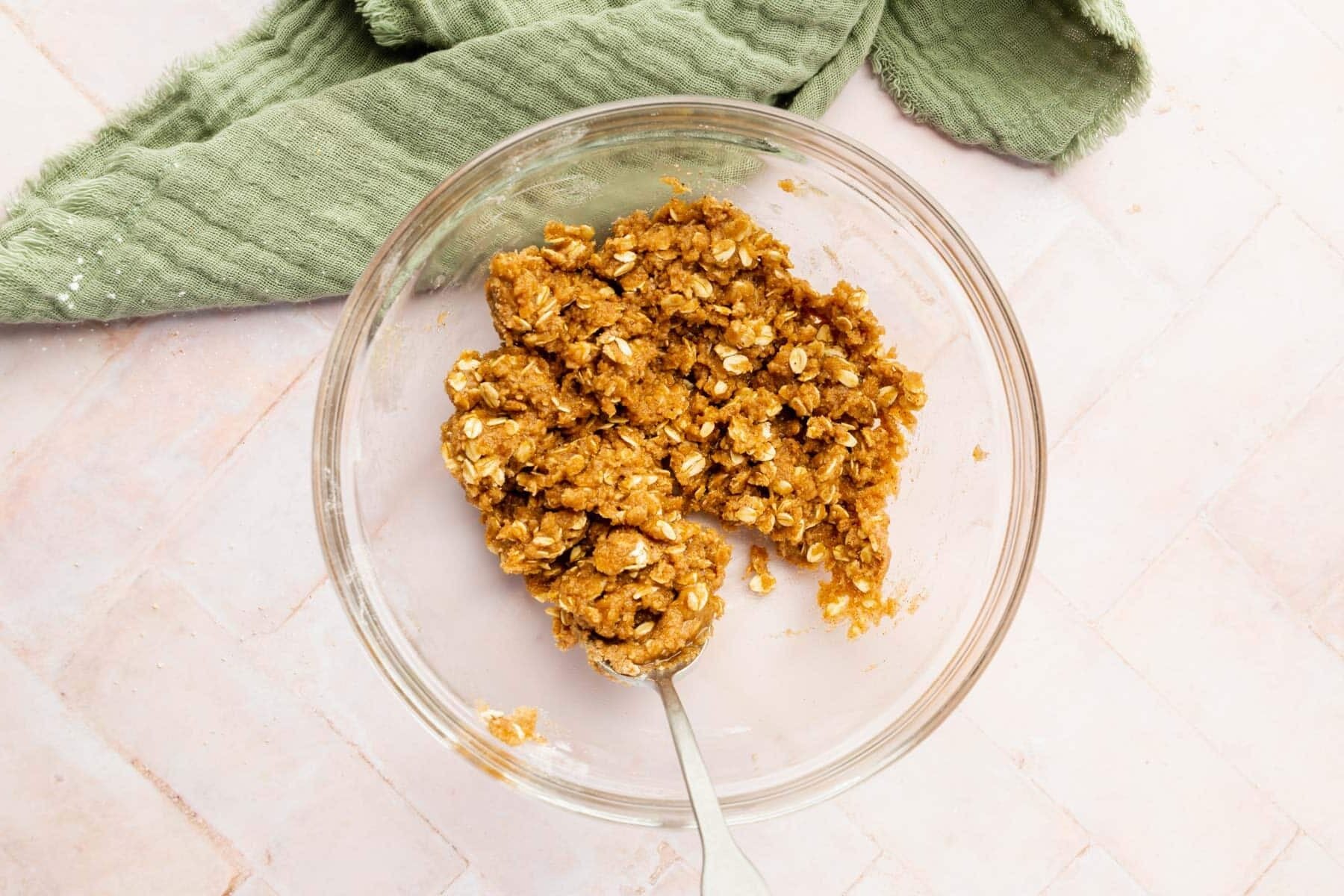 A glass bowl with gluten-free oats, brown sugar, gluten-free flour, melted butter, and spices all mixed together with a spoon.