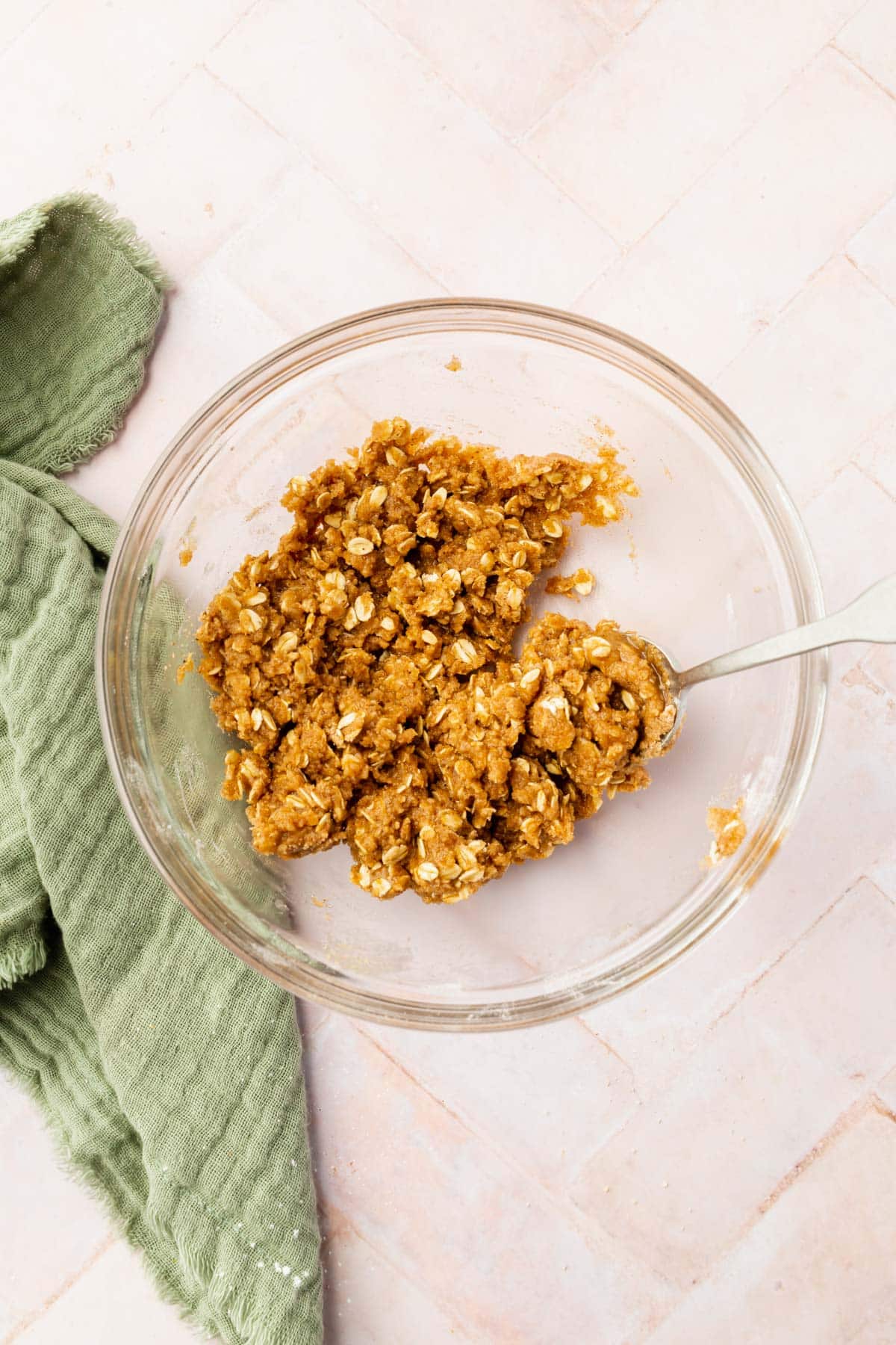 A glass bowl with gluten-free oats, brown sugar, gluten-free flour, melted butter, and spices all mixed together with a spoon.