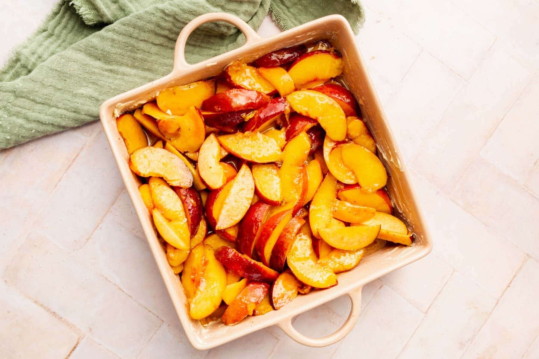 Fresh sliced peaches in a square baking dish tossed with granulated sugar and spices.