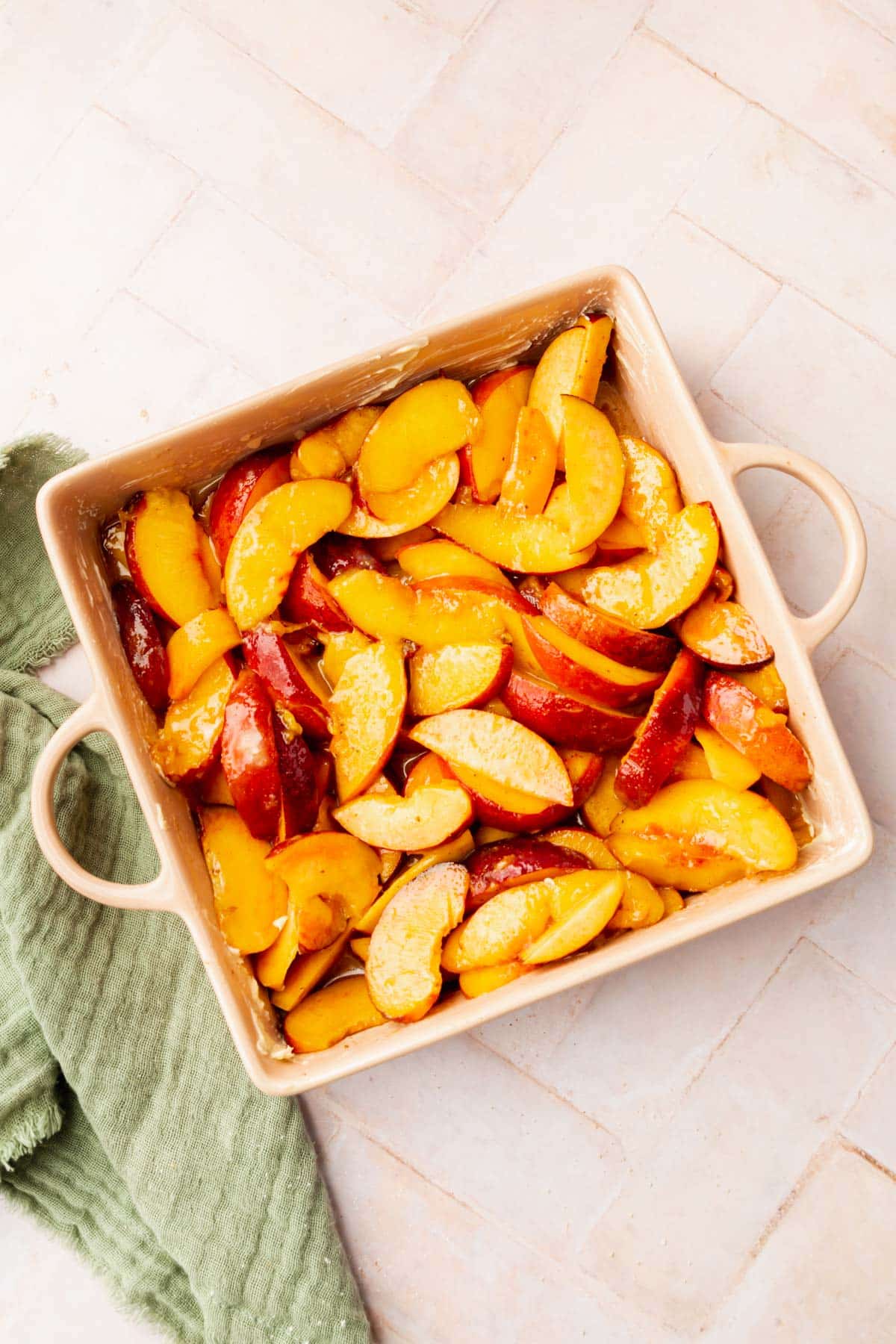 Fresh sliced peaches in a square baking dish tossed with granulated sugar and spices.