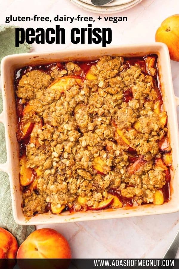 An overhead view of a square baking dish with baked gluten-free peach crisp in it surrounded by fresh peaches.