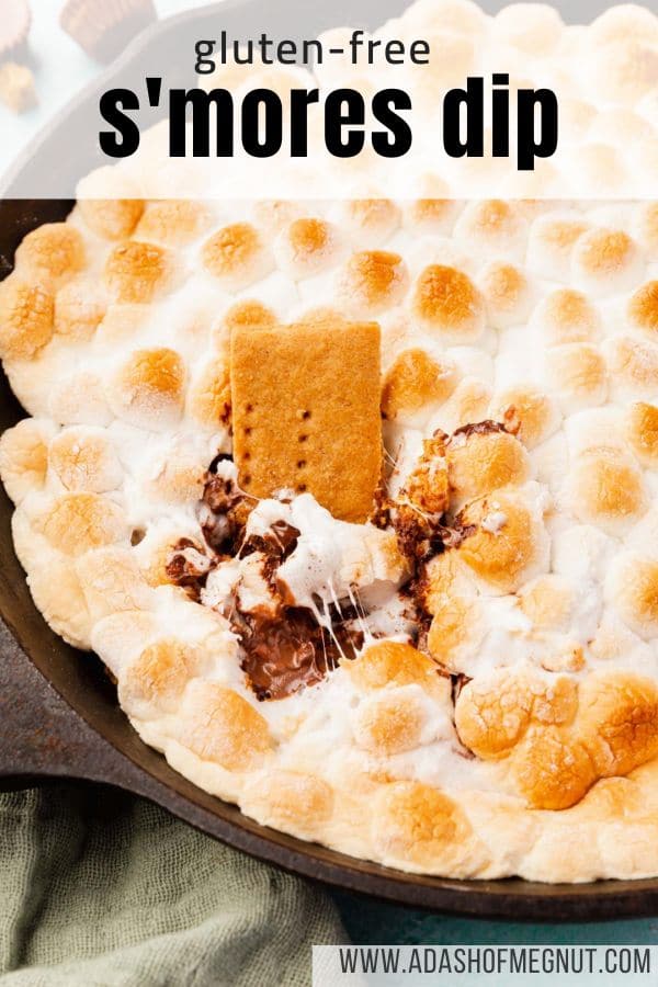 A graham cracker dipped in s'mores dip in a cast iron skillet with a text overlay.