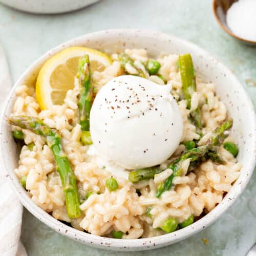 A bowl of pea and asparagus risotto topped with burrata and a lemon wedge.