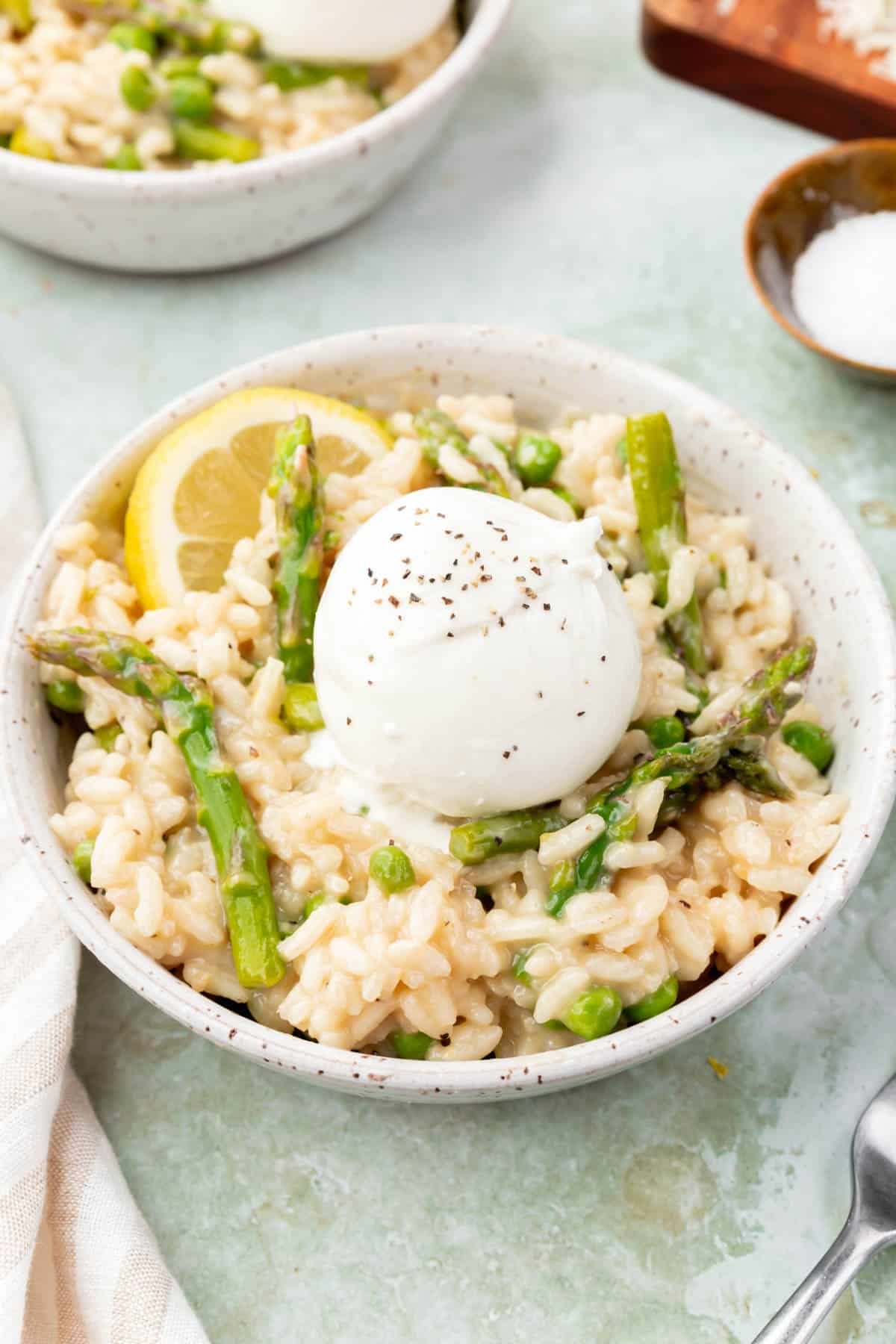 A bowl of pea and asparagus risotto topped with burrata and a lemon wedge.