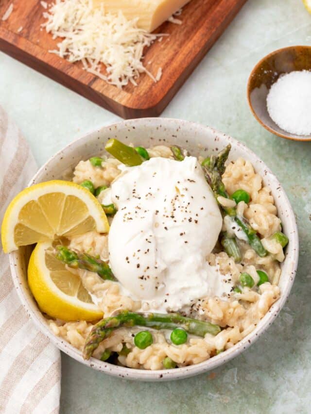 A bowl of risotto with peas, asparagus, burrata and lemon wedges.