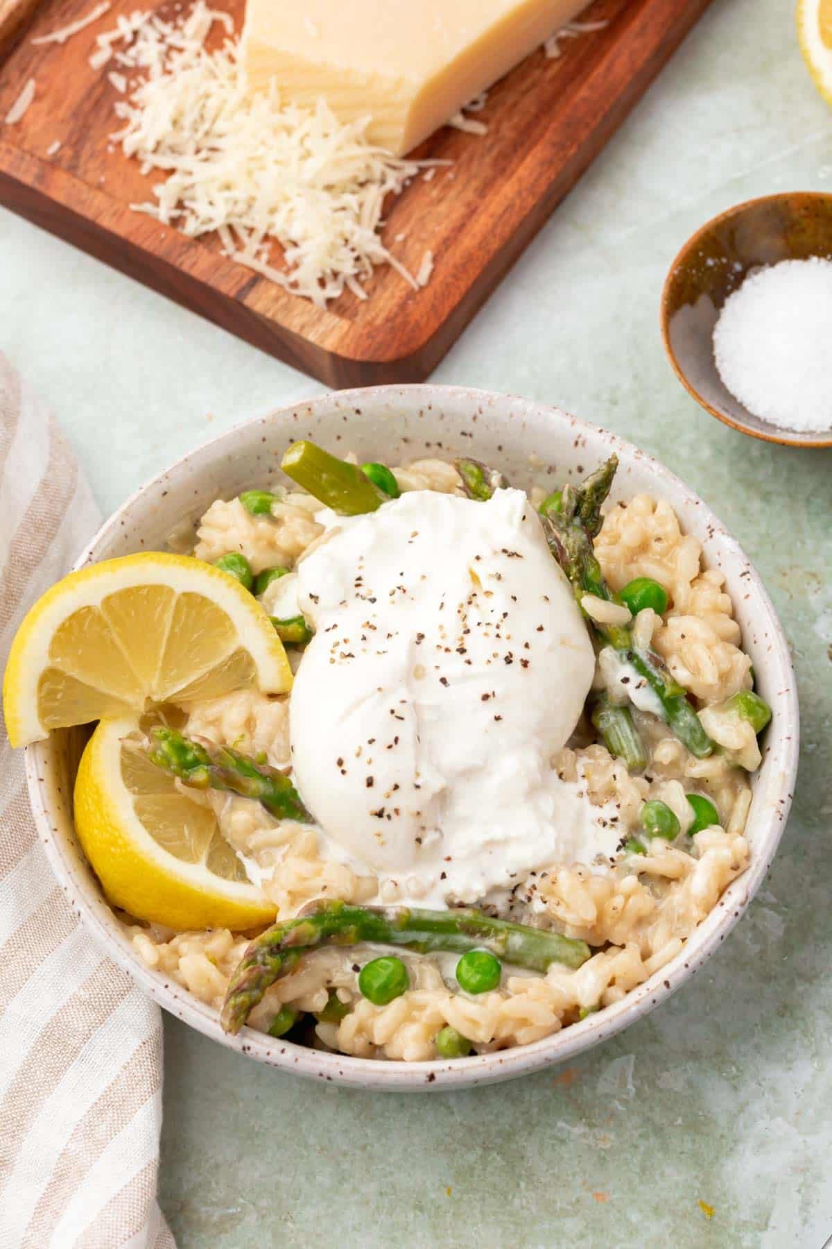 A bowl of risotto with peas, asparagus, burrata and lemon wedges.