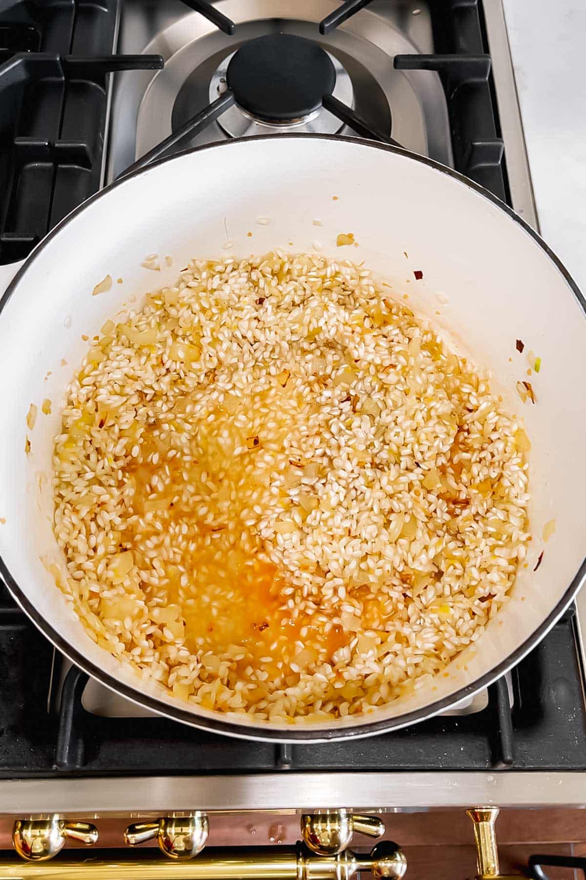 White wine mixed with toasted arborio rice and diced onions in a large dutch oven.