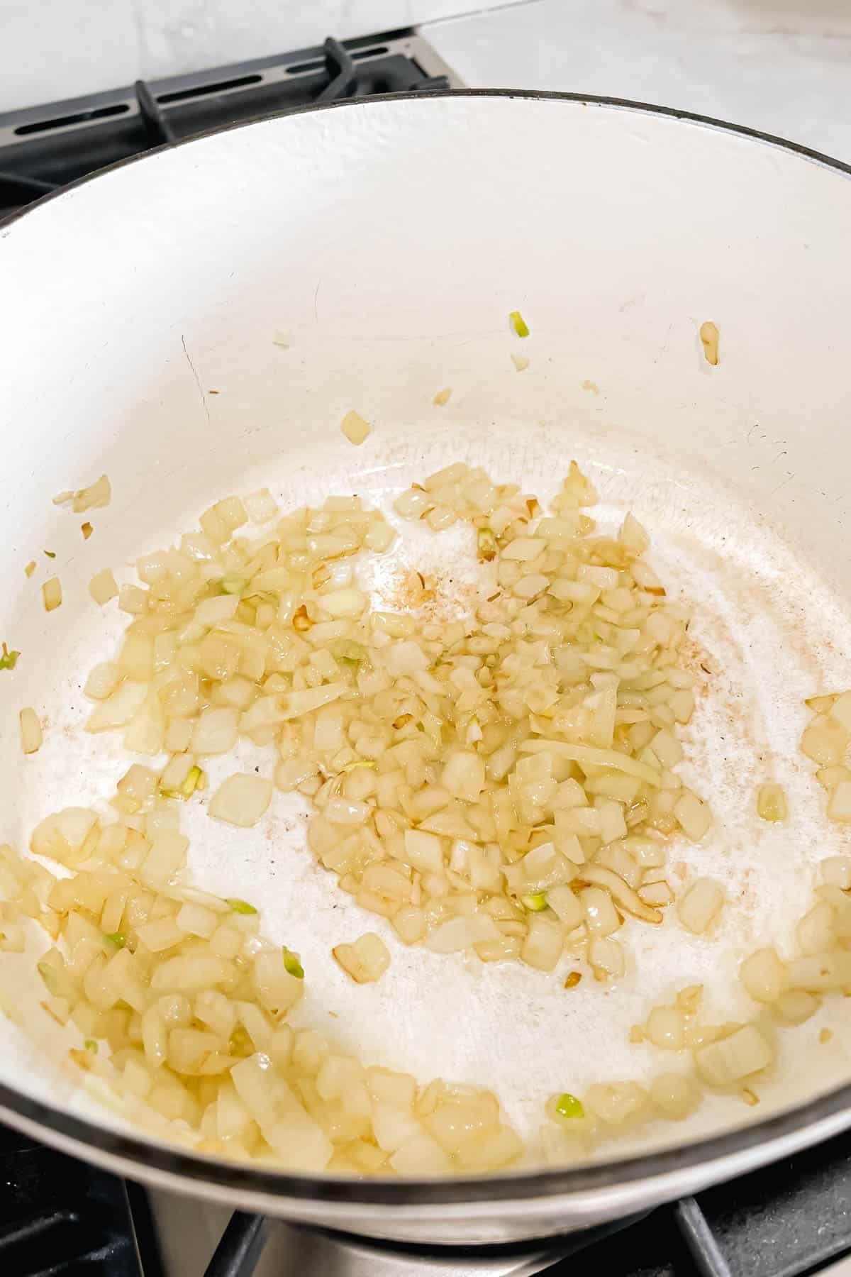 Sautéed diced onions and minced garlic cooking in olive oil in a white dutch oven.