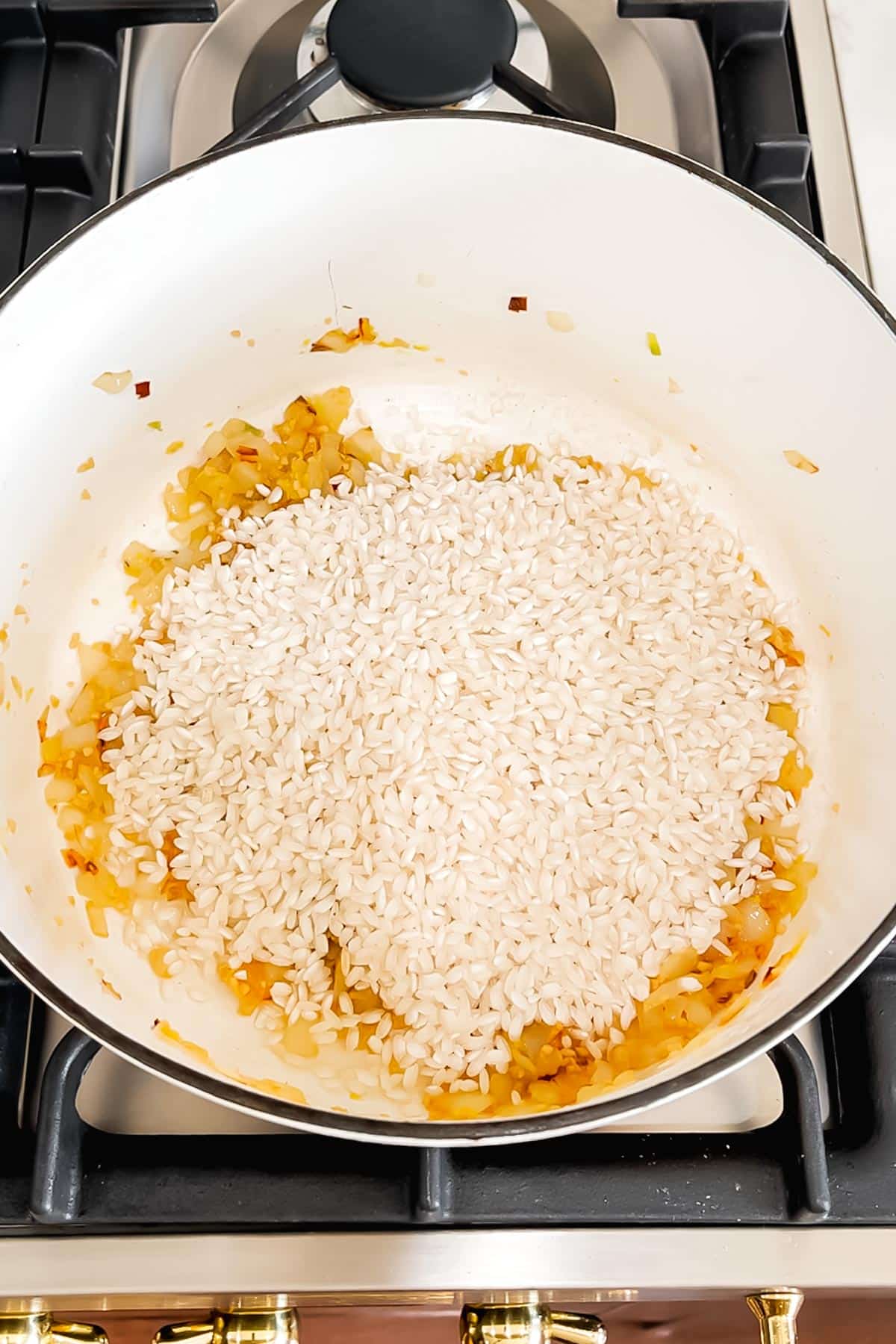 Arborio rice added to a dutch oven with sautéed diced onion.