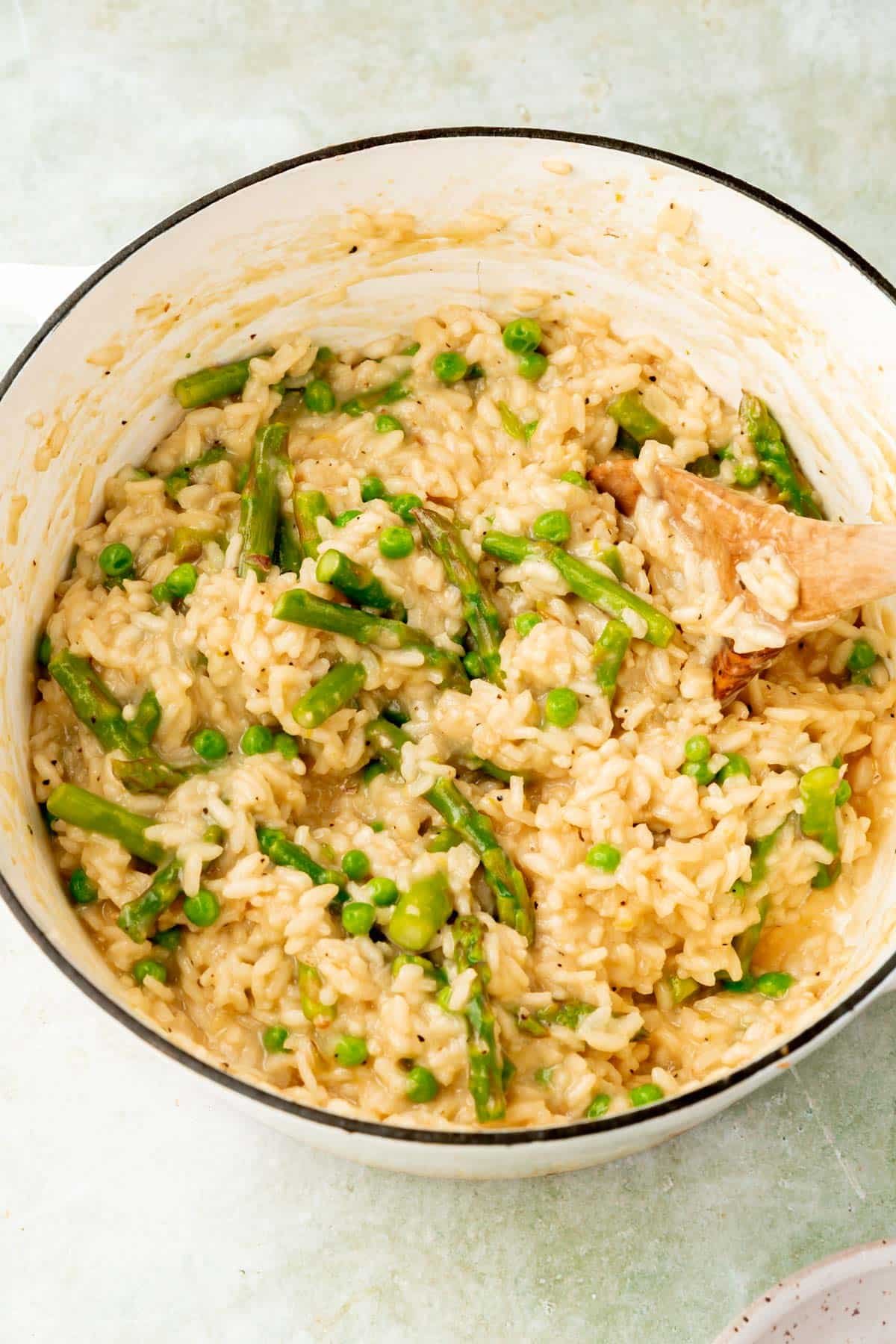Arborio rice mixed with asparagus and peas in a large white dutch oven.