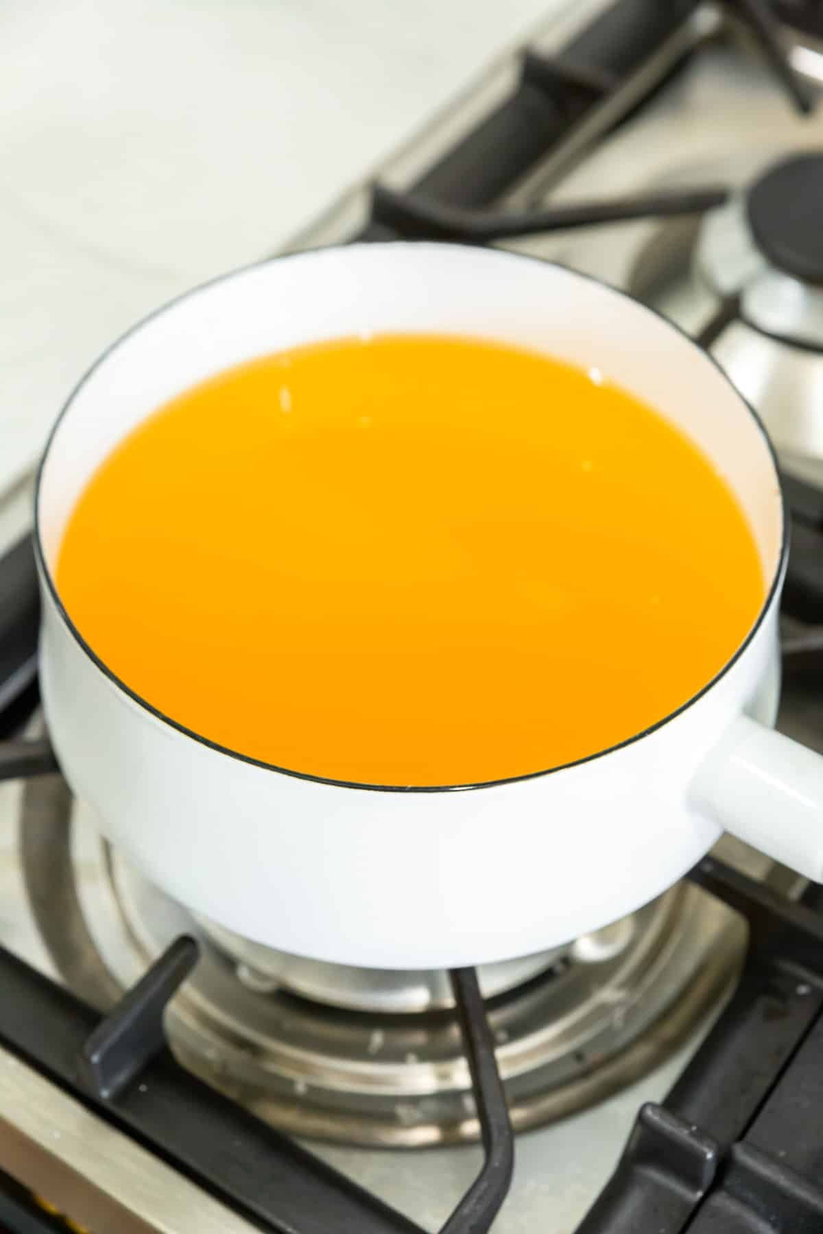 A white saucepan on a stove filled with vegetable stock.