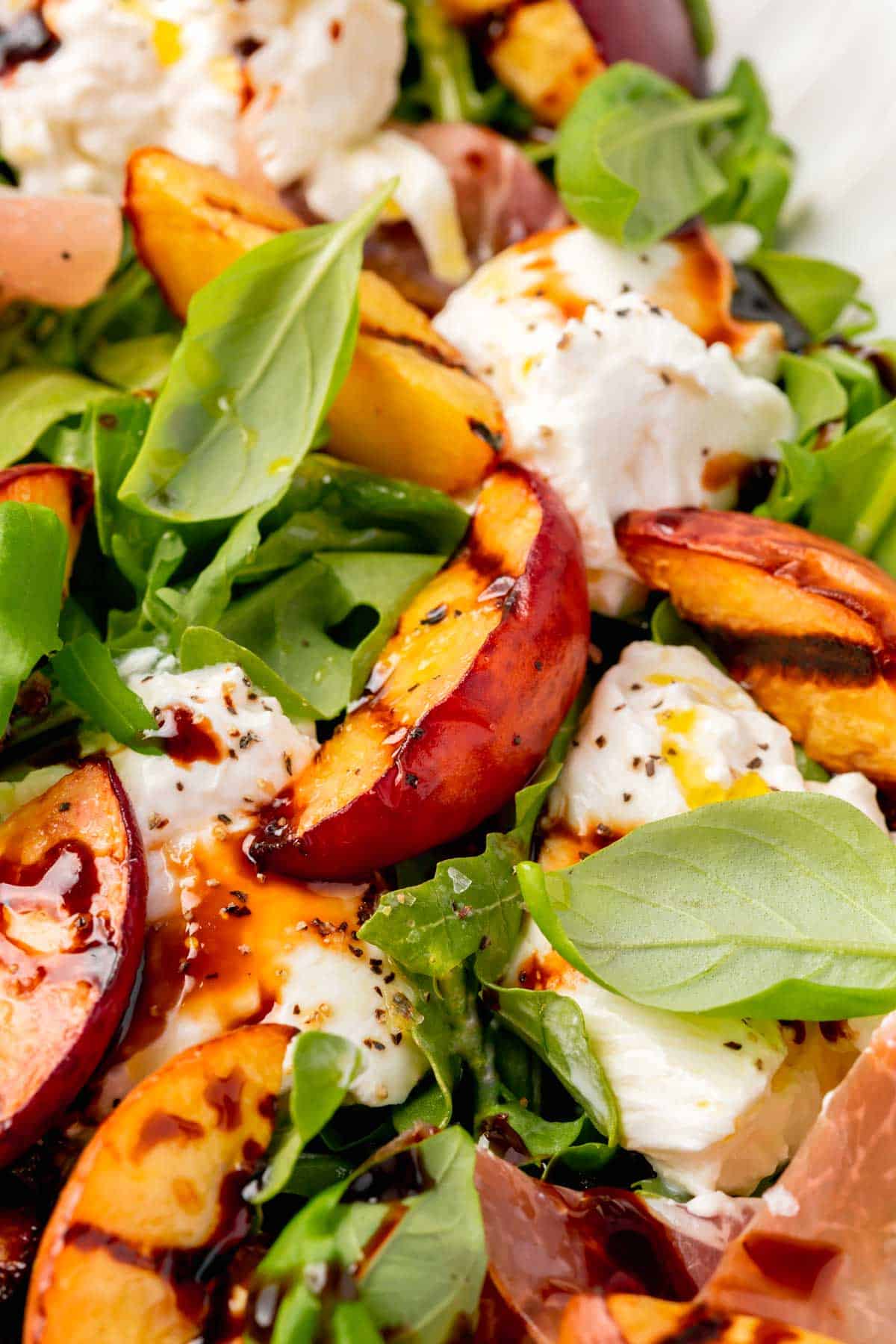 A closeup view of grilled peach arugula salad with burrata, basil and balsamic reductions.