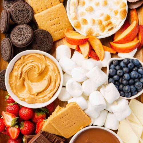 A s'mores board filled with gluten-free oreos, graham crackers, s'mores dip, peaches, blueberries, marshmallows, peanut butter, nutella, strawberries, white chocolate, and marshmallows.