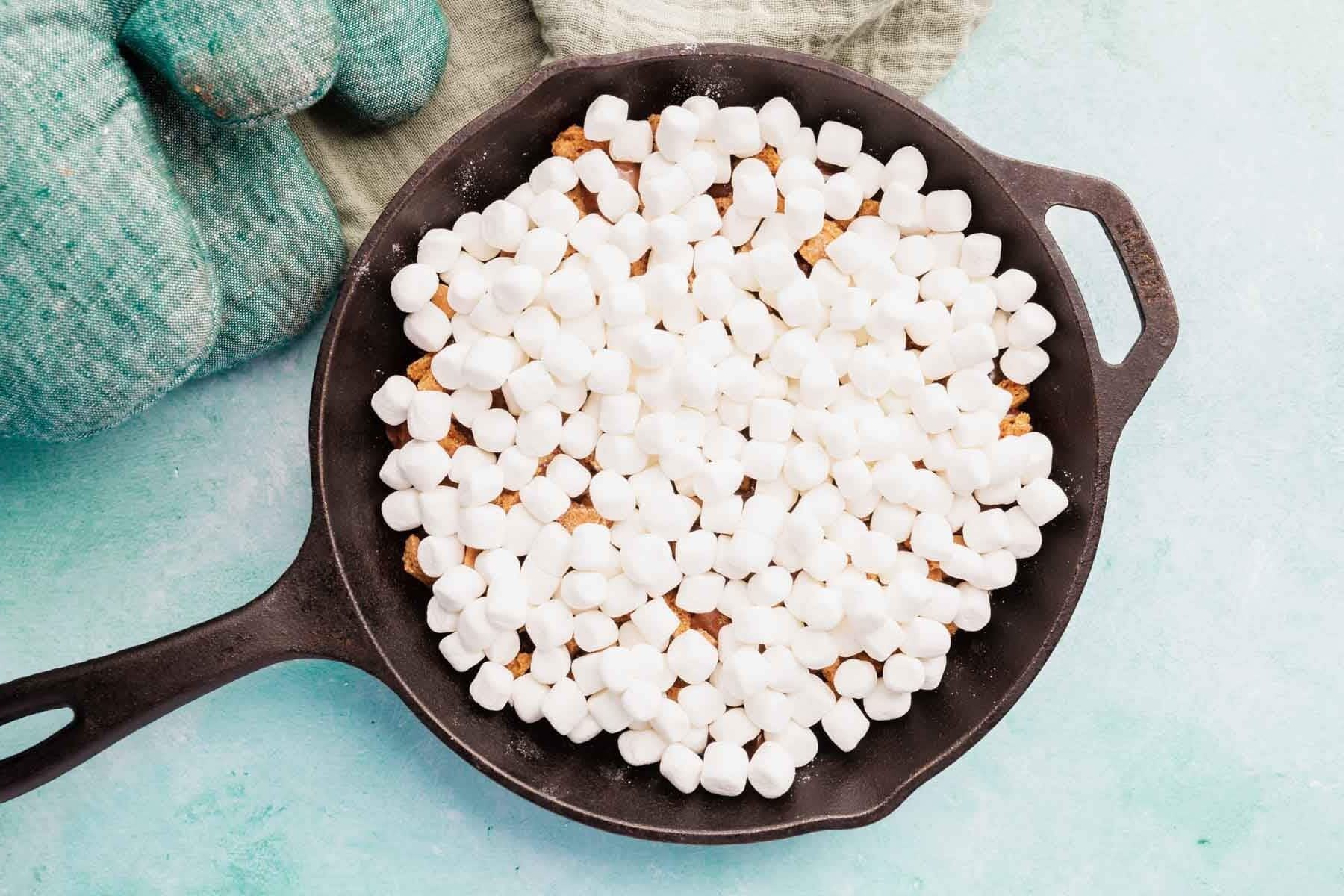 Marshmallows layered over chocolate in a cast iron skillet.
