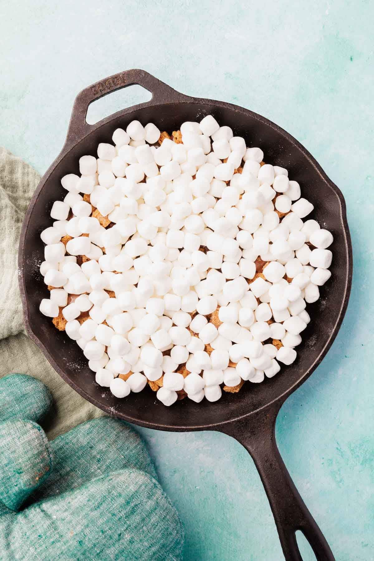 Marshmallows layered over chocolate in a cast iron skillet.