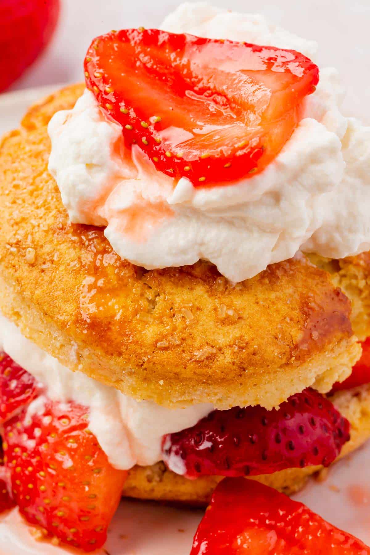 A close up of a gluten-free strawberry shortcake topped with whipped cream and macerated strawberries.