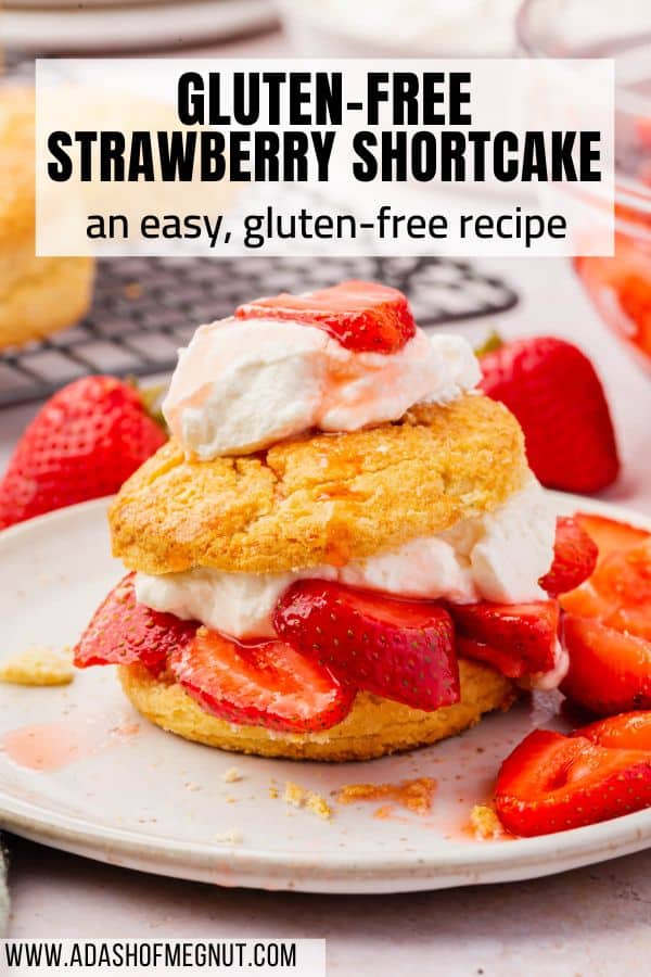 One strawberry shortcake on a plate with a cooling rack of biscuits in the background.