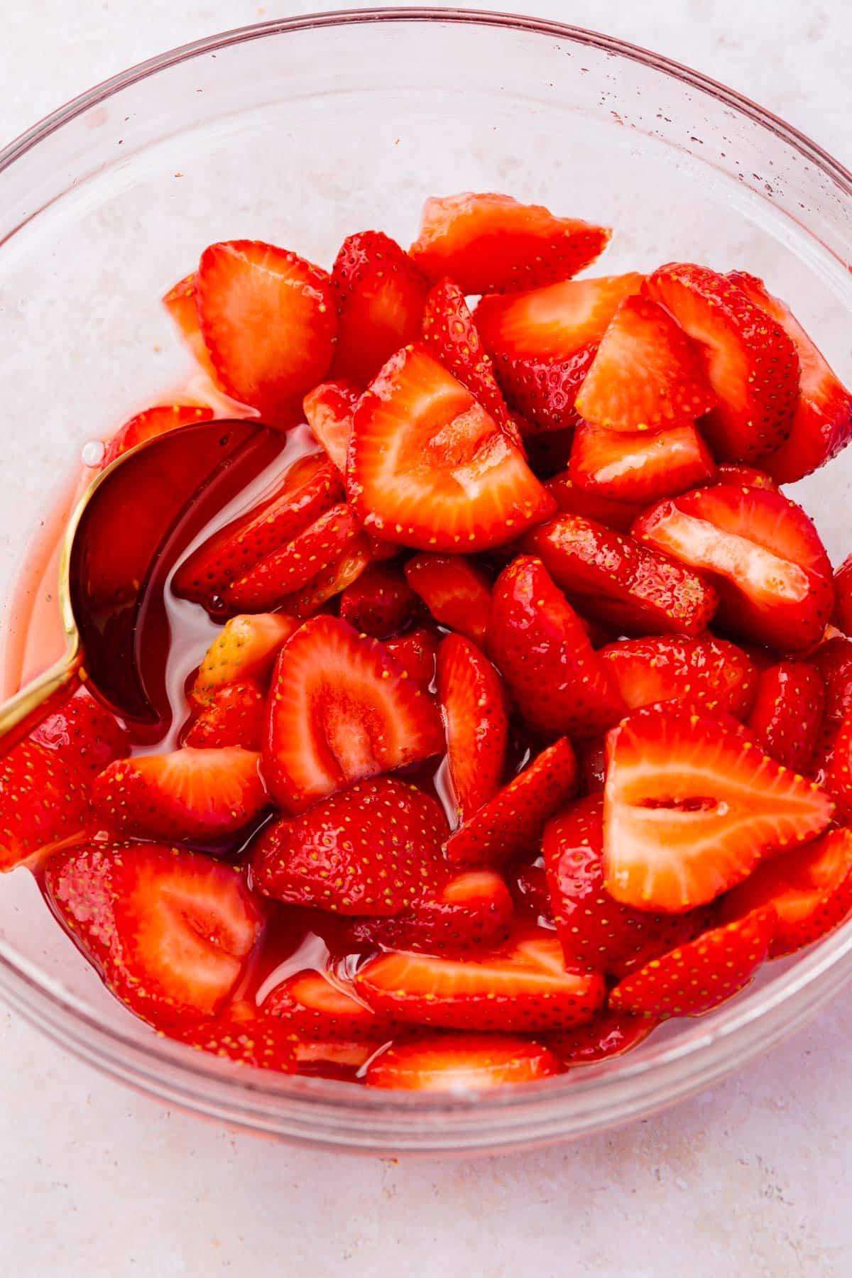 A bowl of macerated strawberries with a gold spoon in it.