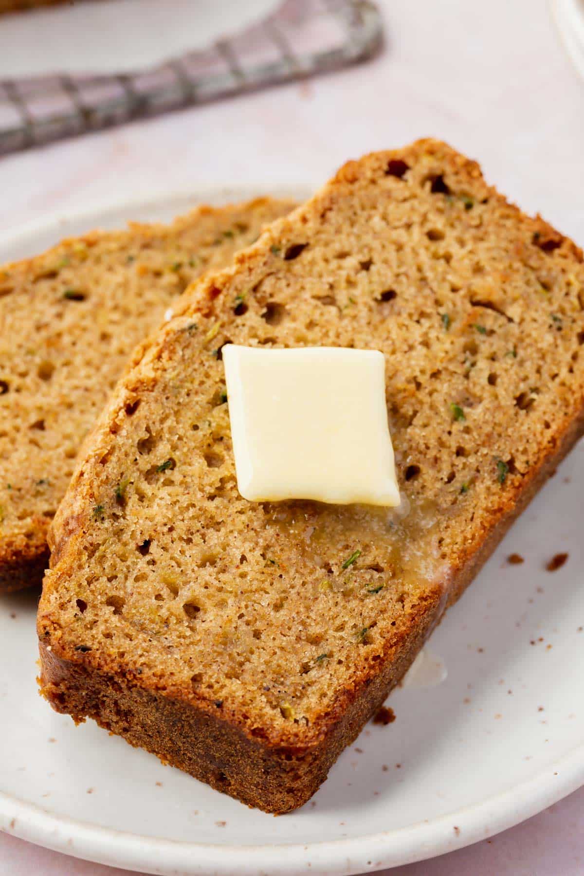 Two slices of gluten-free zucchini bread stacked on a small plate with a slice of melting butter on top.