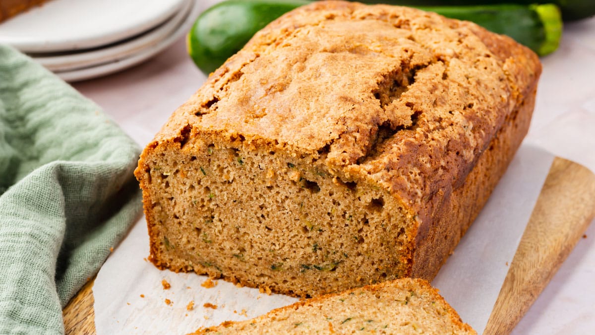 A loaf of gluten-free zucchini bread on a cutting board with one slice cut off.
