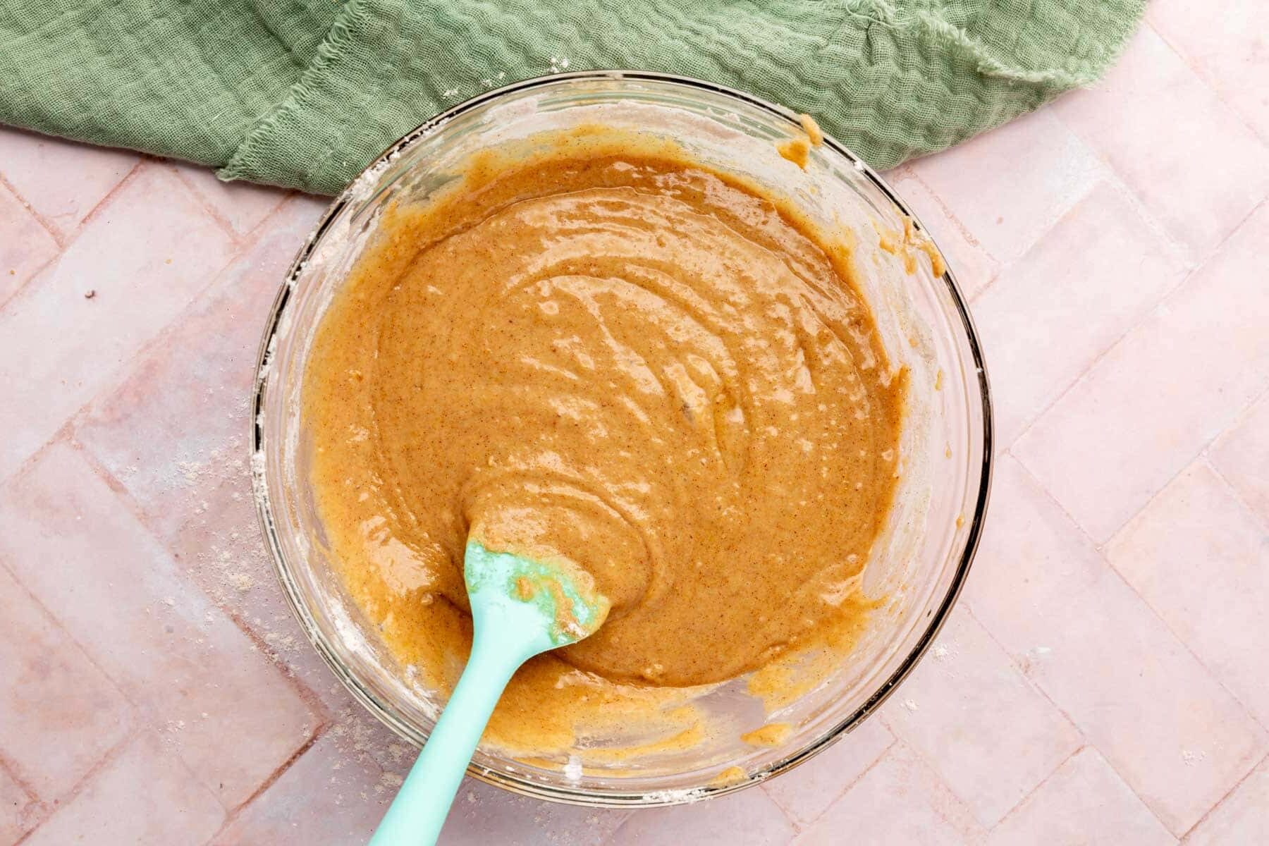 Wet ingredients in a glass bowl with a blue spatula to make gluten-free zucchini bread.