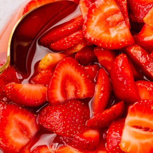 A close up of macerated strawberries in a glass bowl with a spoon.