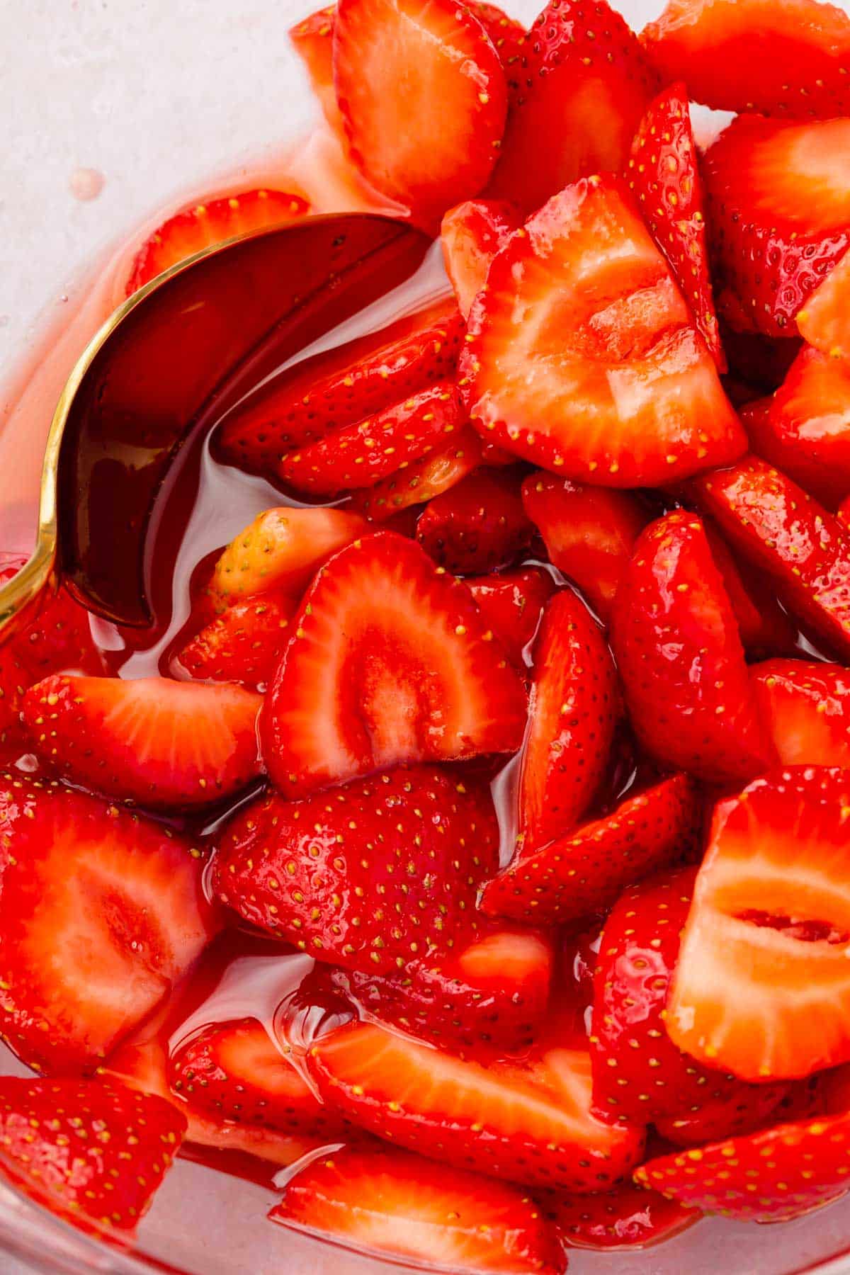 A close up of macerated strawberries in a glass bowl with a spoon.