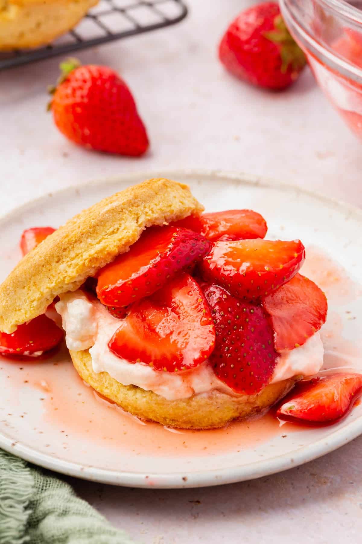 A closeup of a sliced gluten-free biscuit topped with whipped cream and sliced macerated strawberries.