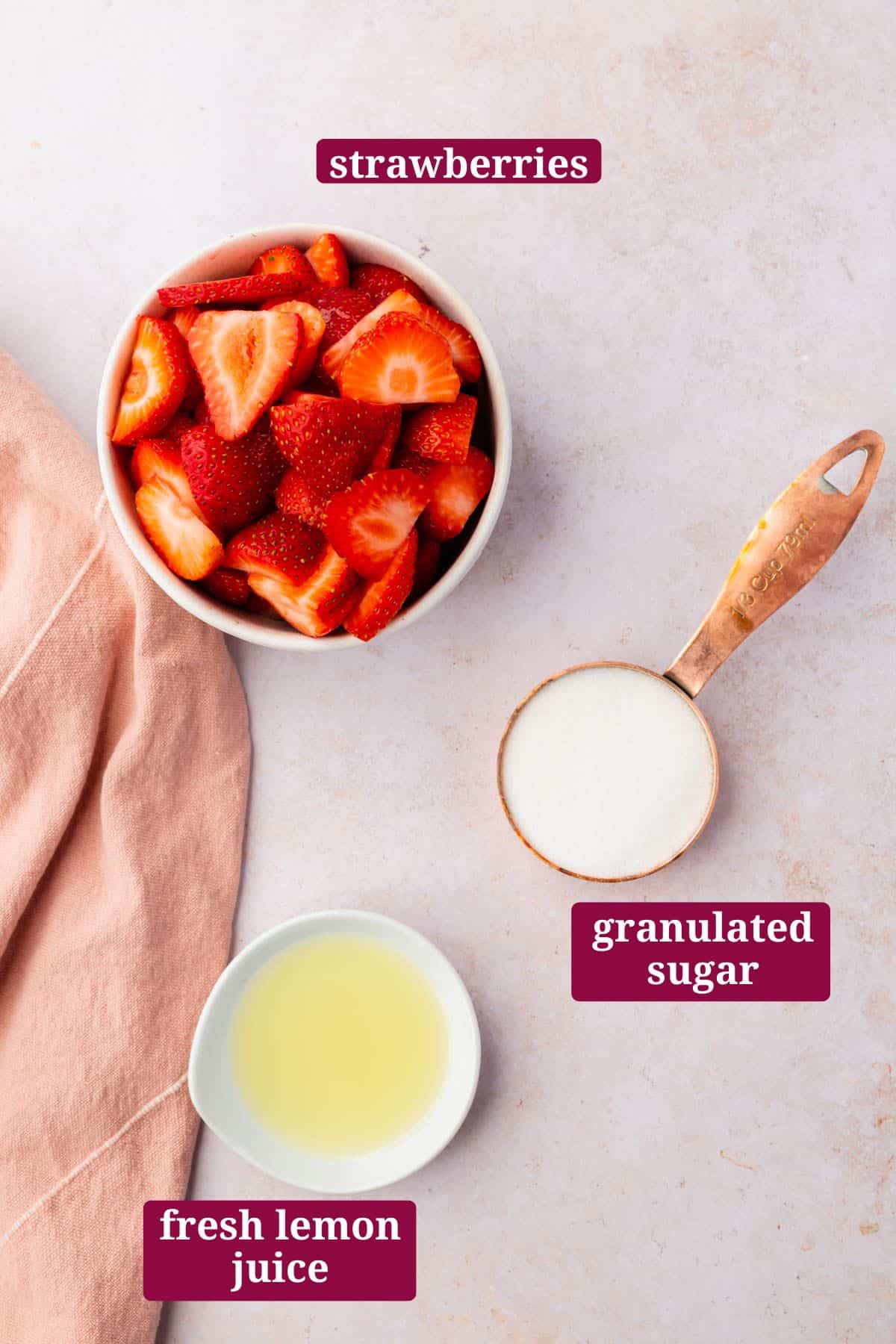 An overhead view of a bowl of sliced strawberries, a small bowl of lemon juice, and a measuring cup of granulated sugar with text overlays over each ingredient.