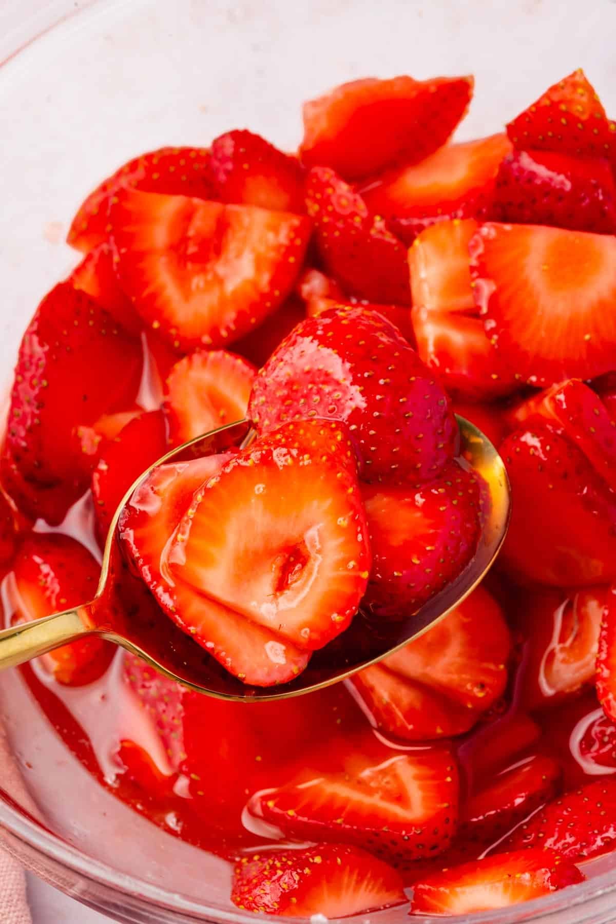 A spoon scooping out macerated strawberries from a larger bowl.