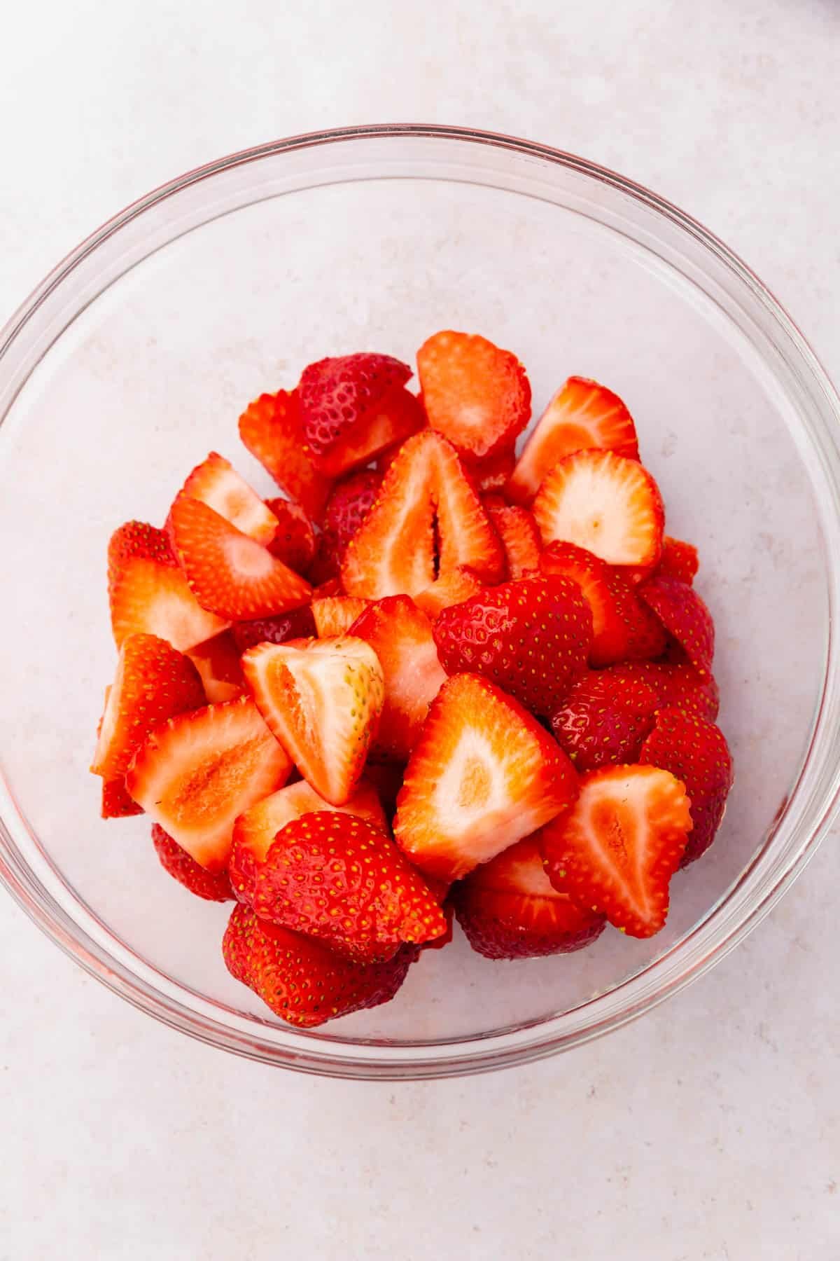 A glass mixing bowl with sliced strawberries in it.