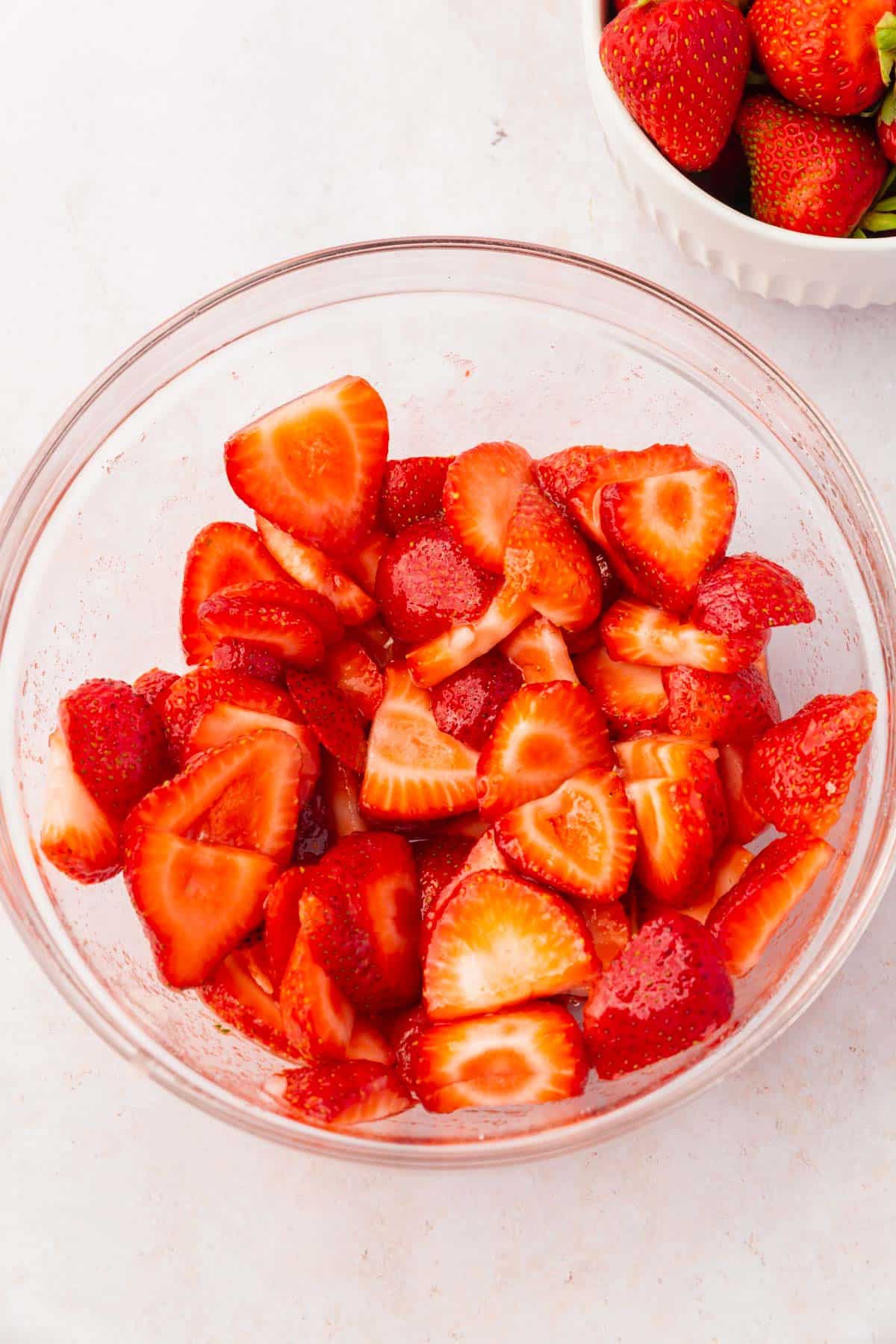 A glass mixing bowl with sliced strawberries that have been tossed with granulated sugar and lemon juice.