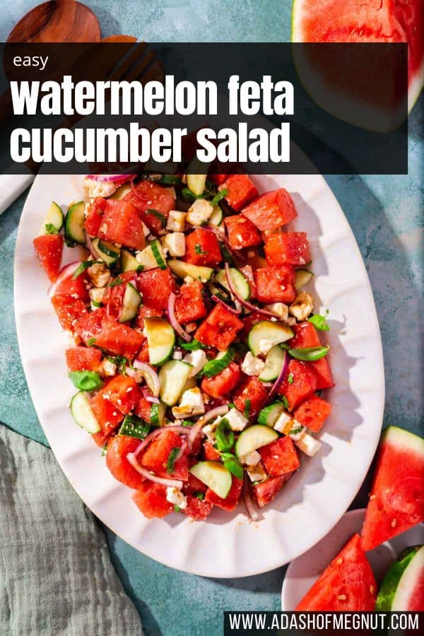 A large oval scalloped platter with watermelon cucumber salad on it topped with basil.