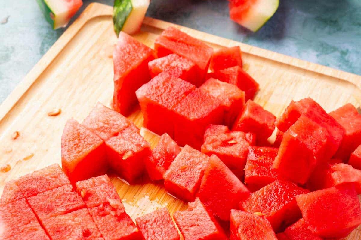 Watermelon cut into cubes on a wood cutting board.