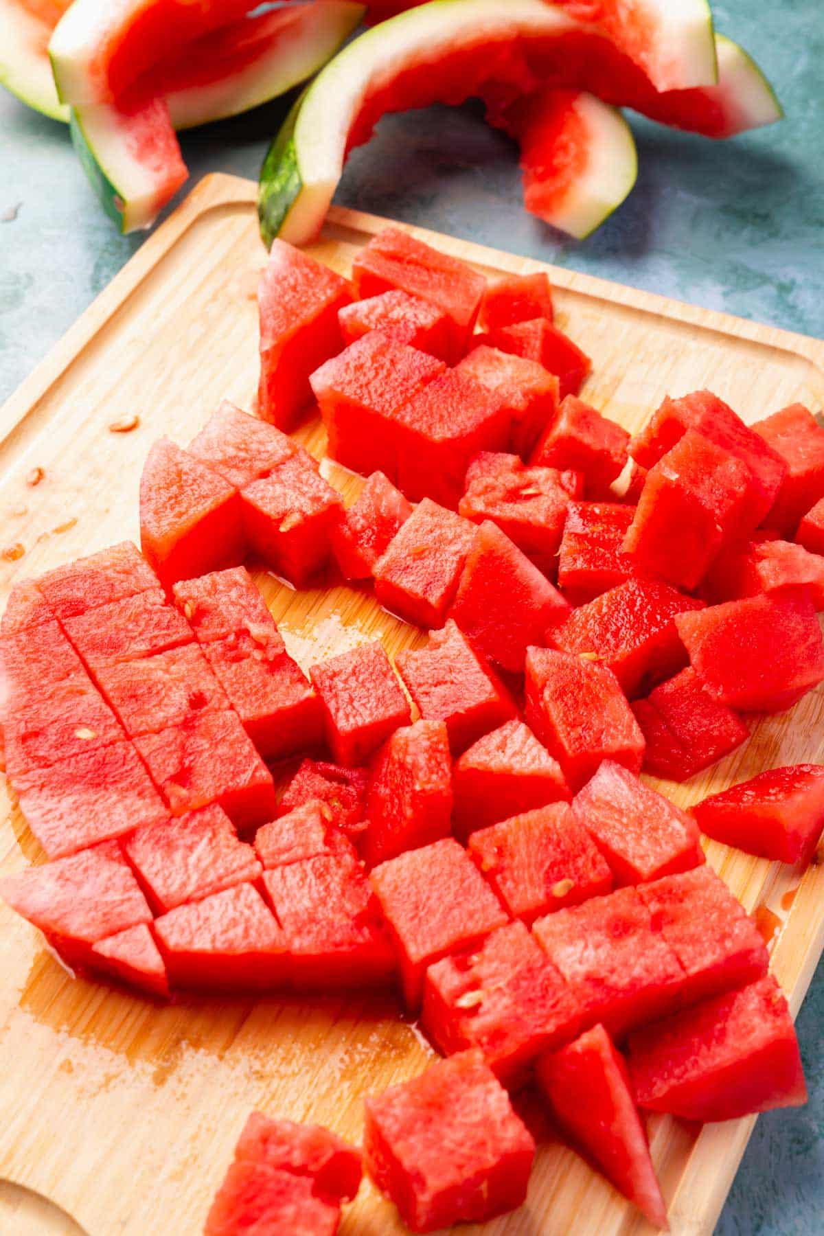 Watermelon cut into cubes on a wood cutting board.