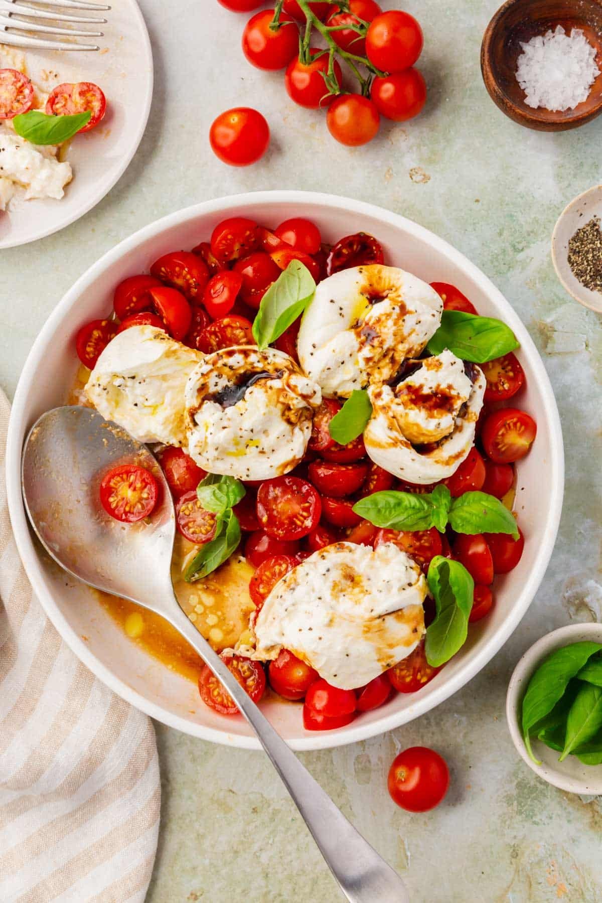 An overhead view of a bowl of burrata caprese salad with a spoon in the bowl.
