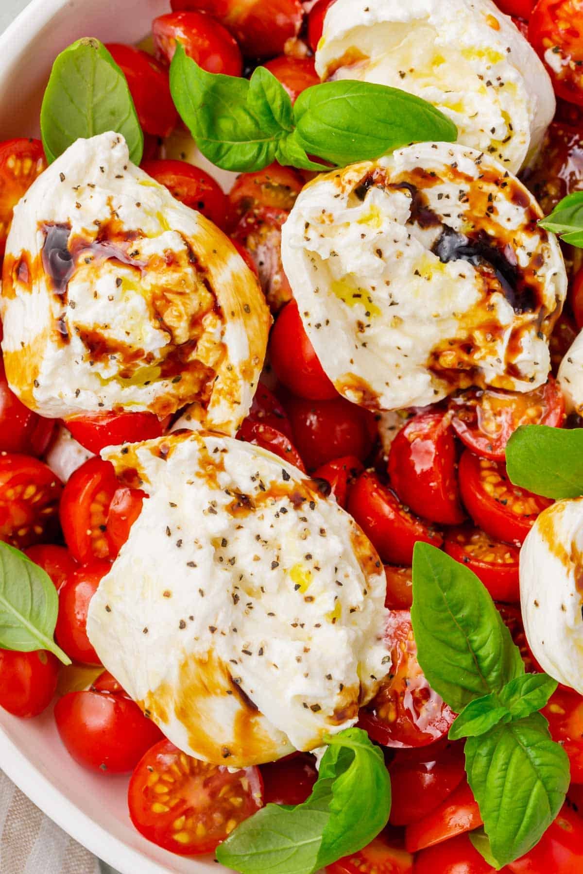 A closeup of burrata caprese salad topped with balsamic glaze and basil leaves.