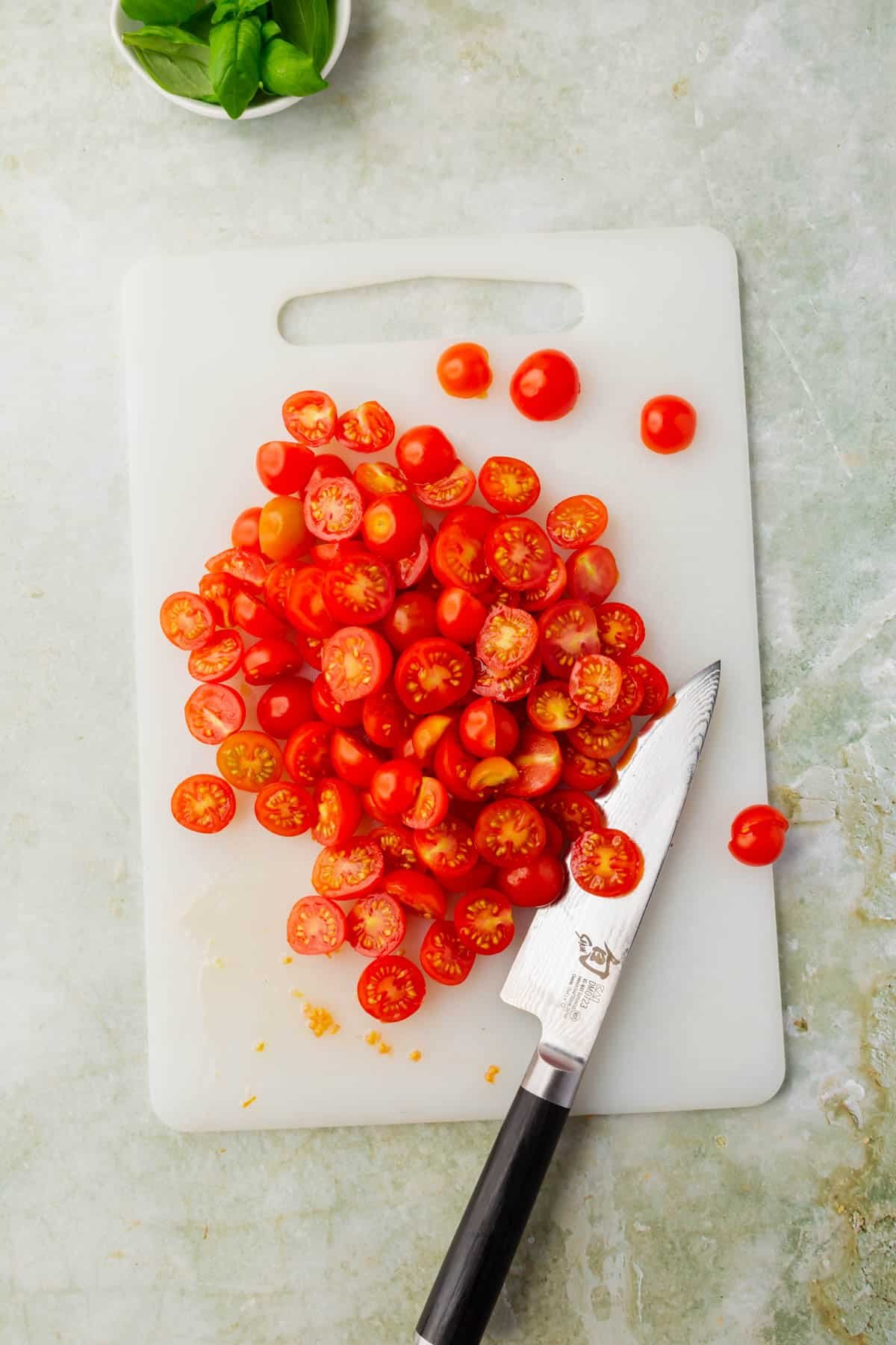 A white cutting board with sliced cherry tomatoes and a knife.