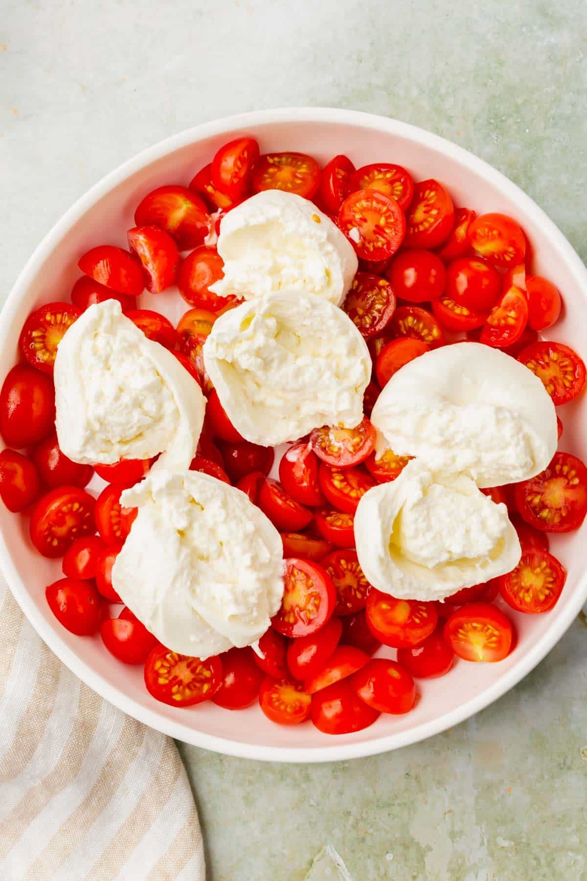 An overhead view of a shallow bowl with sliced cherry tomatoes and burrata cheese.