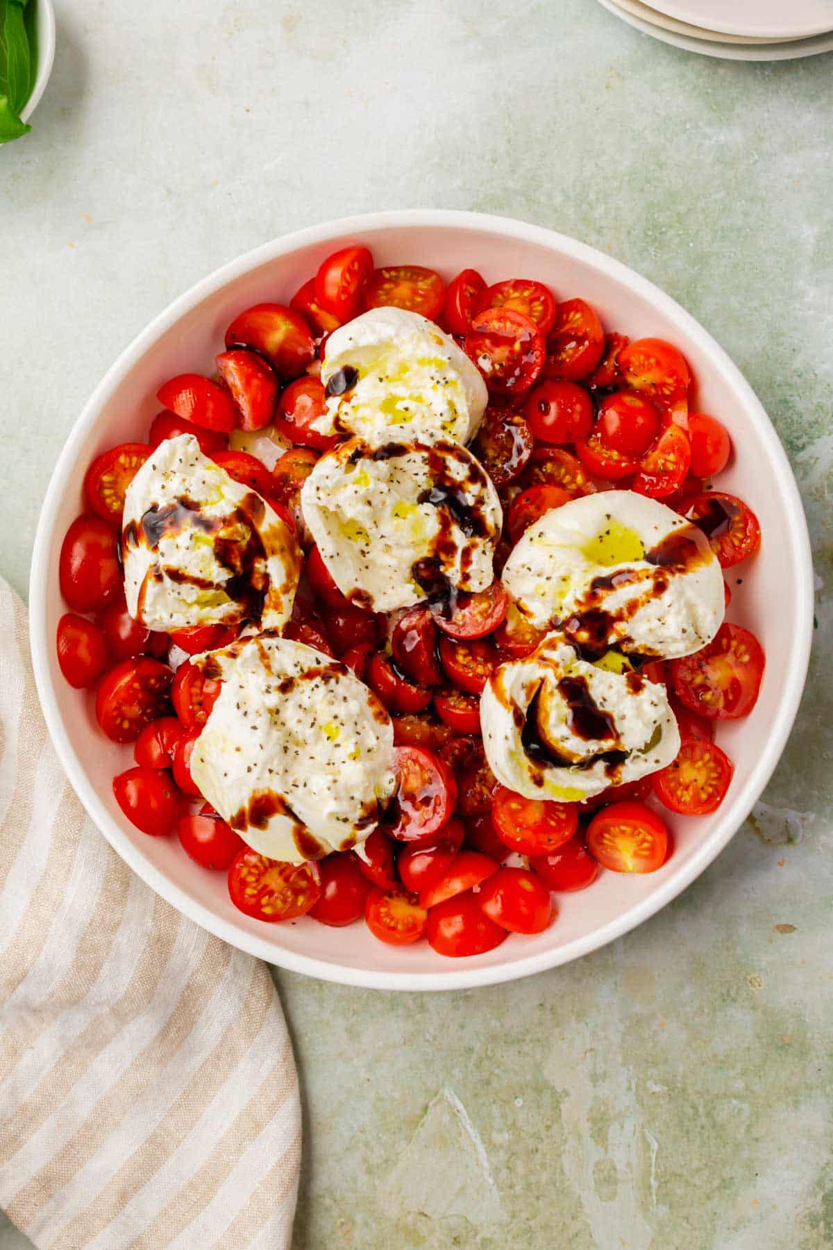 An overhead shot of a shallow bowl of sliced cherry tomatoes topped with burrata cheese, olive oil and balsamic glaze.