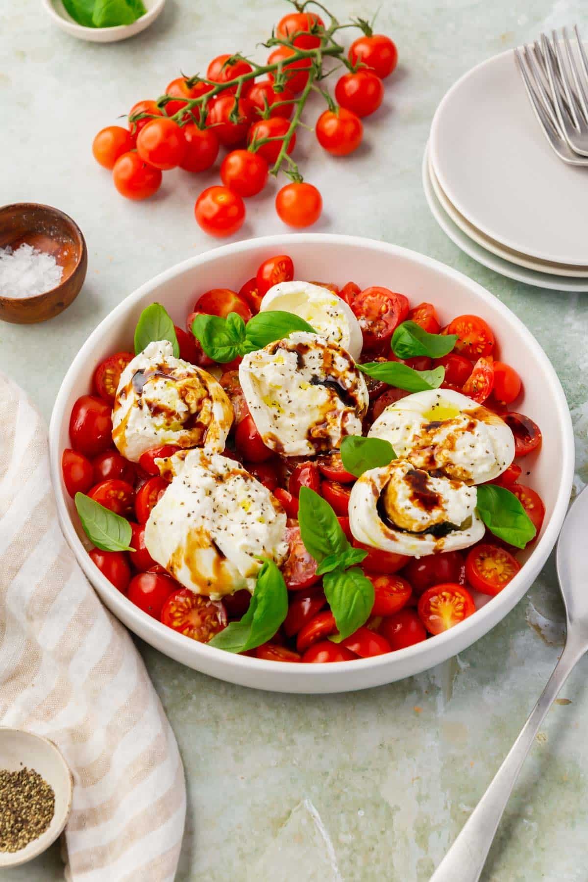 A shallow bowl of burrata caprese topped with basil with cherry tomatoes in the background.
