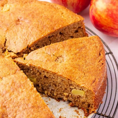 A close up of a round gluten-free apple cake with a wedge sliced from it.