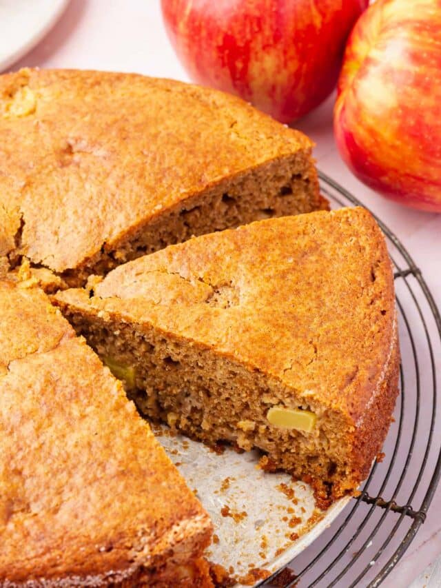 A close up of a round gluten-free apple cake with a wedge sliced from it.