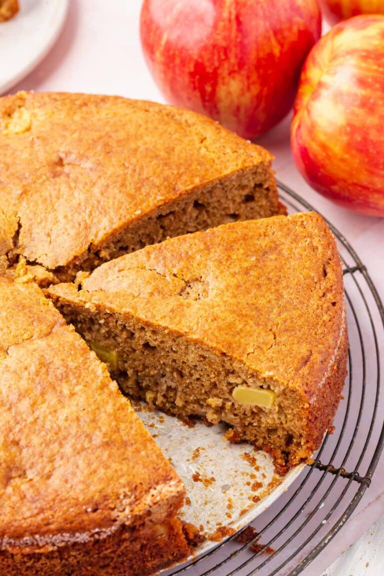 A close up of a round gluten-free apple cake with a wedge sliced from it.