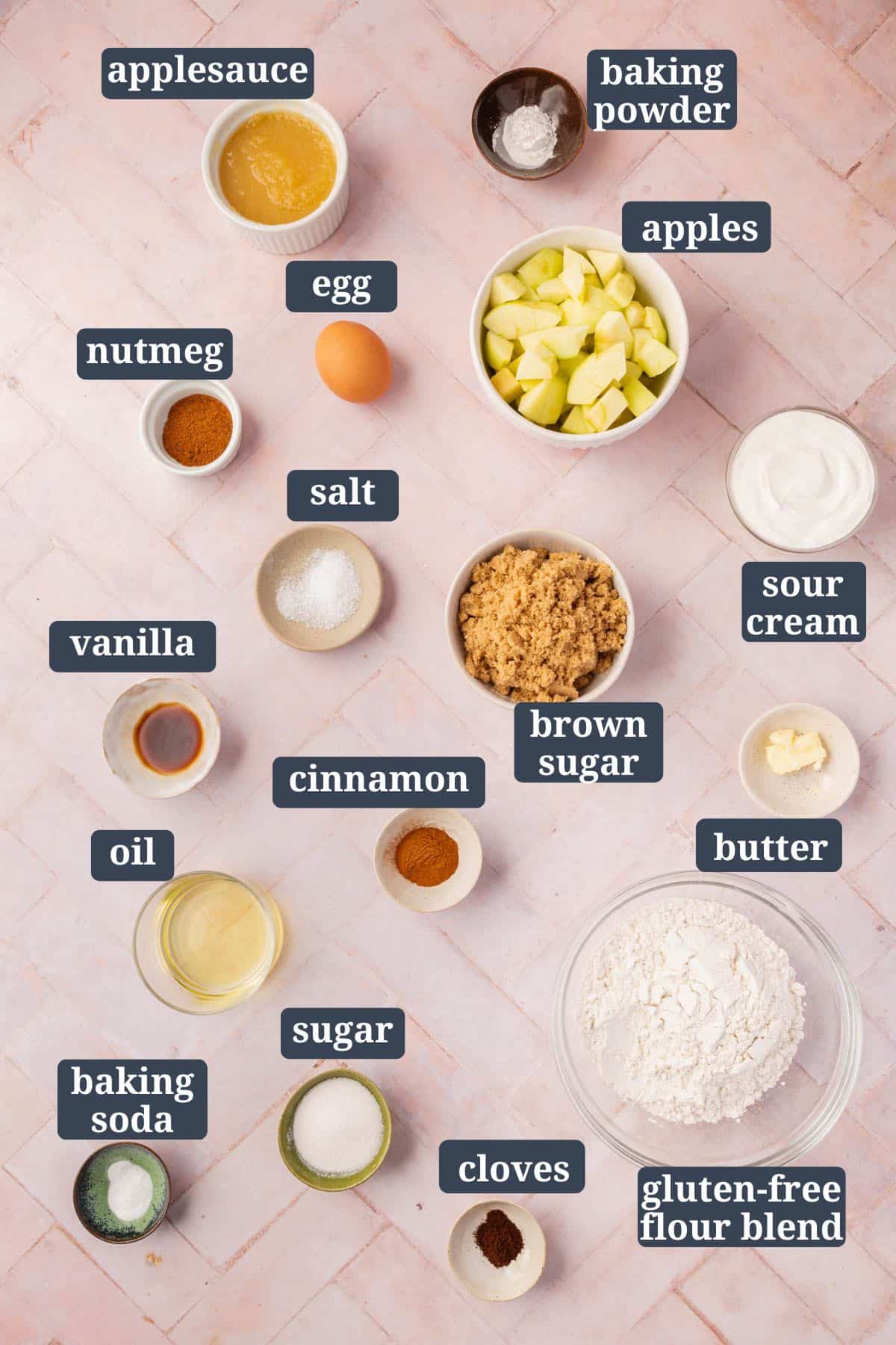 An overhead view of ingredients in bowls on a pink table to make gluten-free apple cake with text overlays over each ingredient.